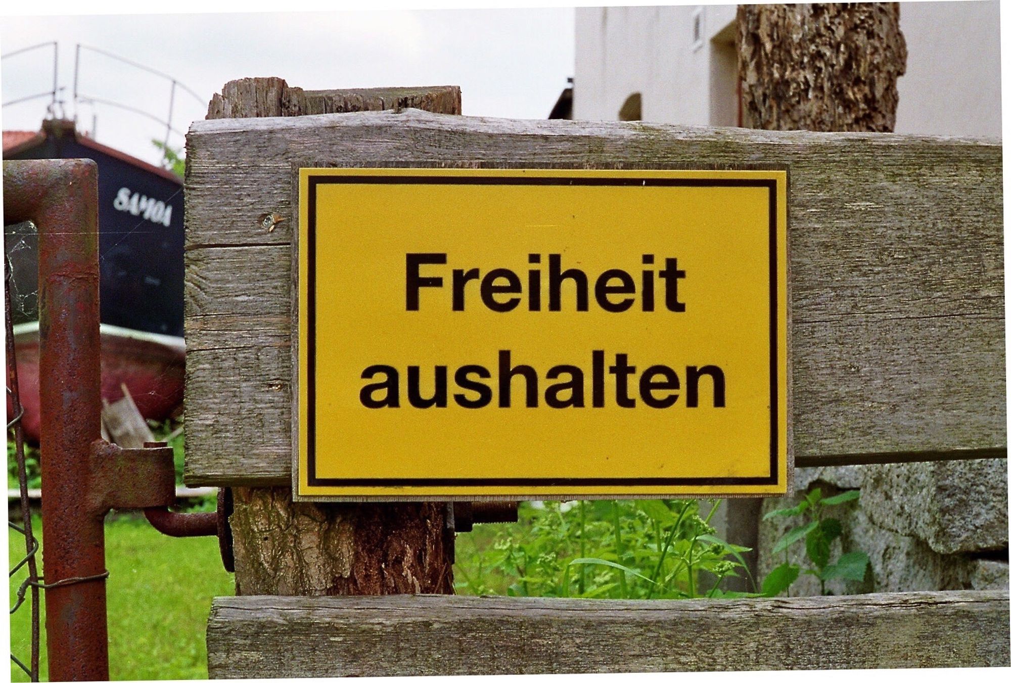 Ein Gatenzaun aus Holz mit einem Schild dran: „Freiheit aushalten“