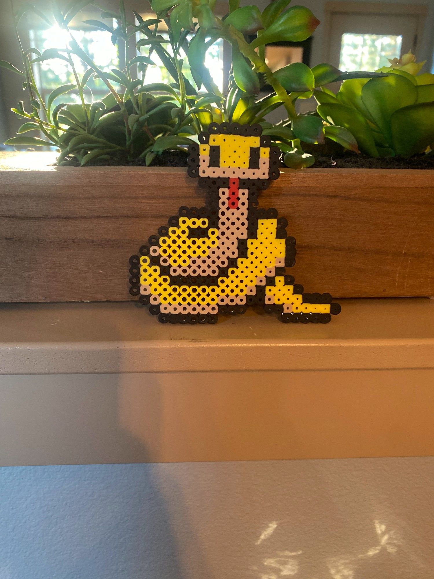 a yellow and cream snake, coiled up with tongue out, made from perler beads.