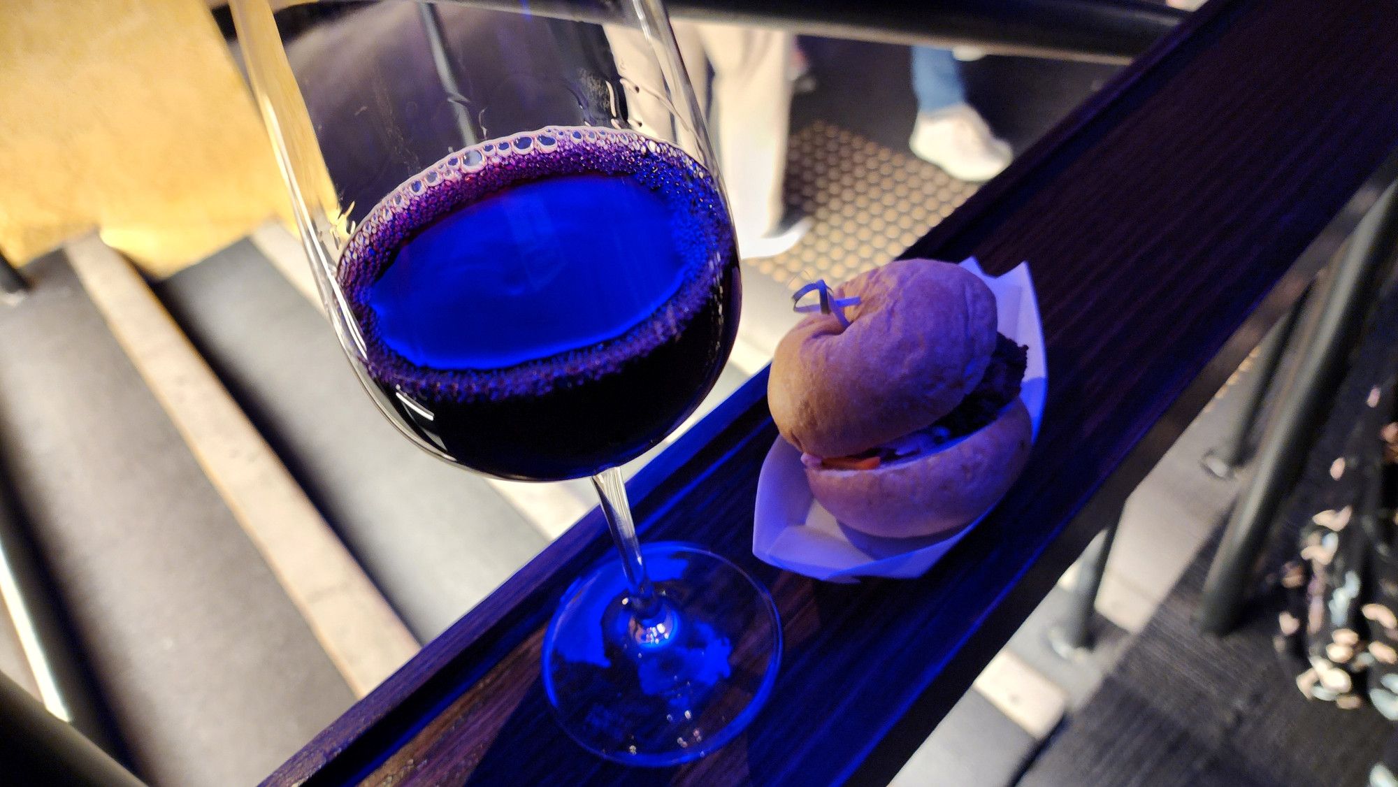 A photo of a glass of red wine and a wagyu cheeseburger slider precariously balanced on a wooden railing next to some stairs. This was my second glass of red and my embarrassingly large number that I refuse to disclose slider.