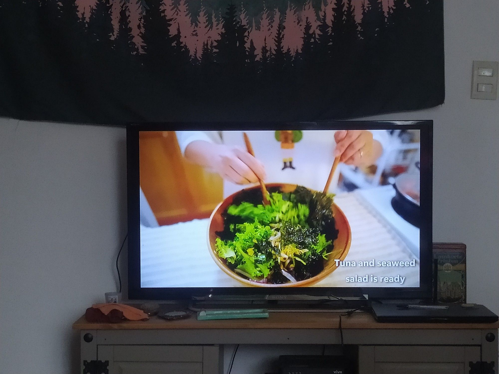 prato de salada de folhas verdes e uma pessoa misturando tudo com duas colheres de pau