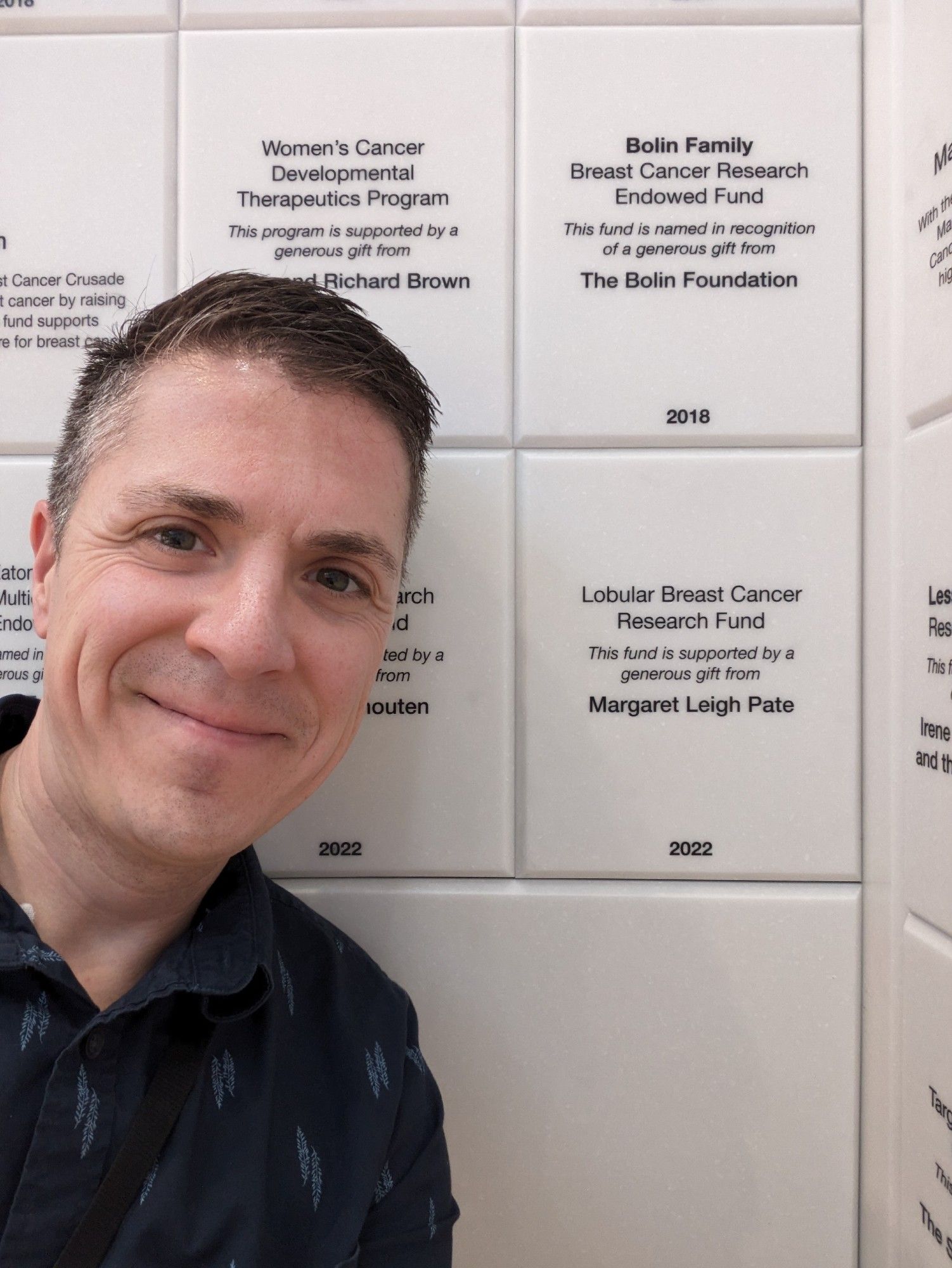 Dr. Sikora next to a donor plaque, reading "Lobular Breast Cancer Research Fund. This fund is supported by a generous gift from Margaret Leigh Pate. 2022."