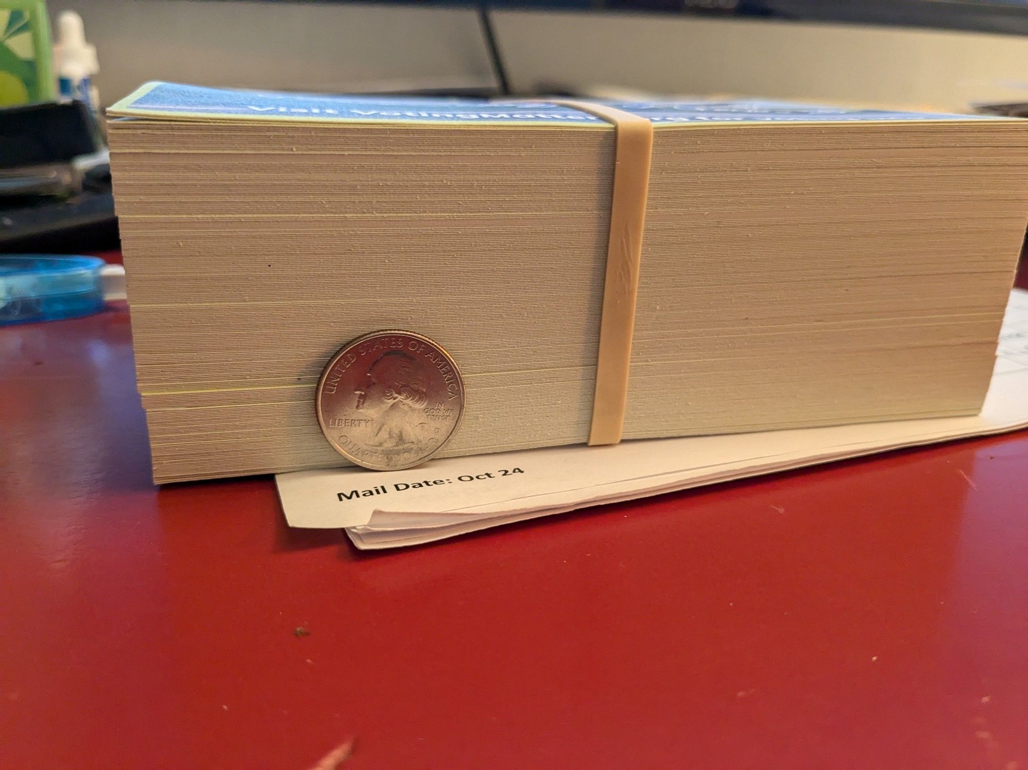 A stack of 194 postcards held together by a rubber band and a quarter for scale.