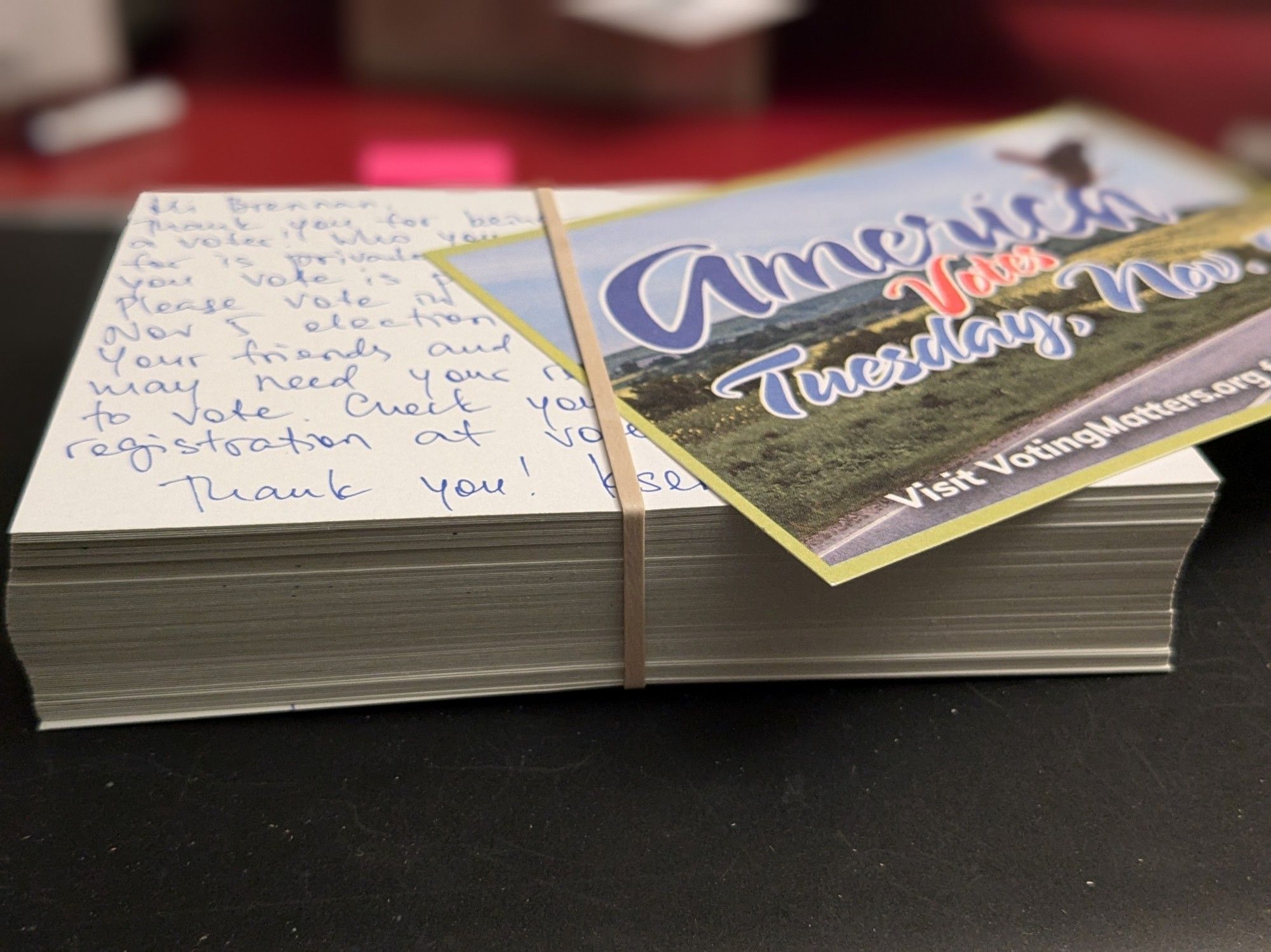 A stack of handwritten postcards held together with a rubber band and an extra postcard front side up covering the address part.