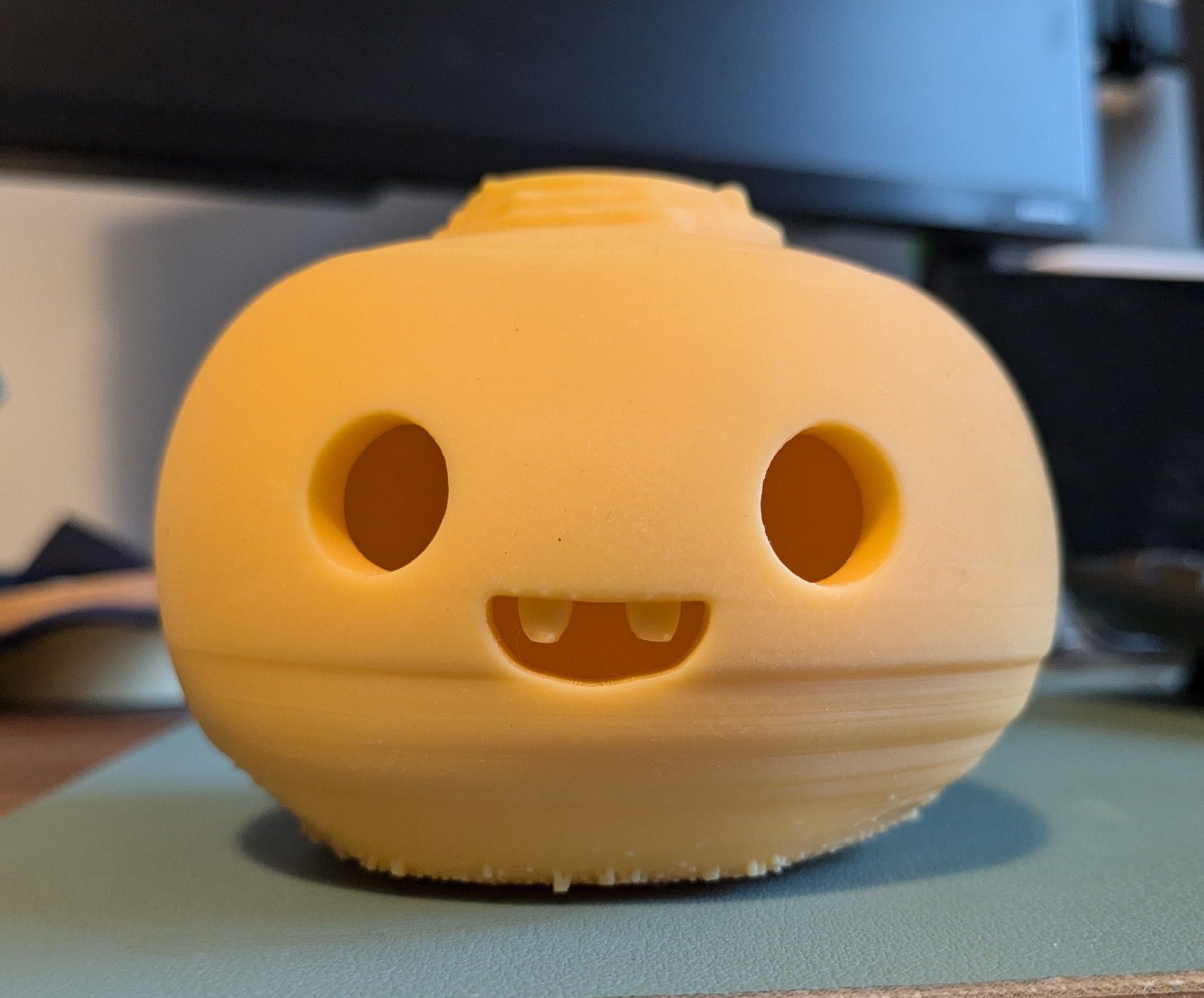 A little neepy lantern (turnip jack-o'-lantern for the non-Scots), 3d printed in yellow resin and as yet un-painted. It has a cute, smiling face with wee stubby fangs. The bottom half is riddled with wobbly layers that printed out of alignment.