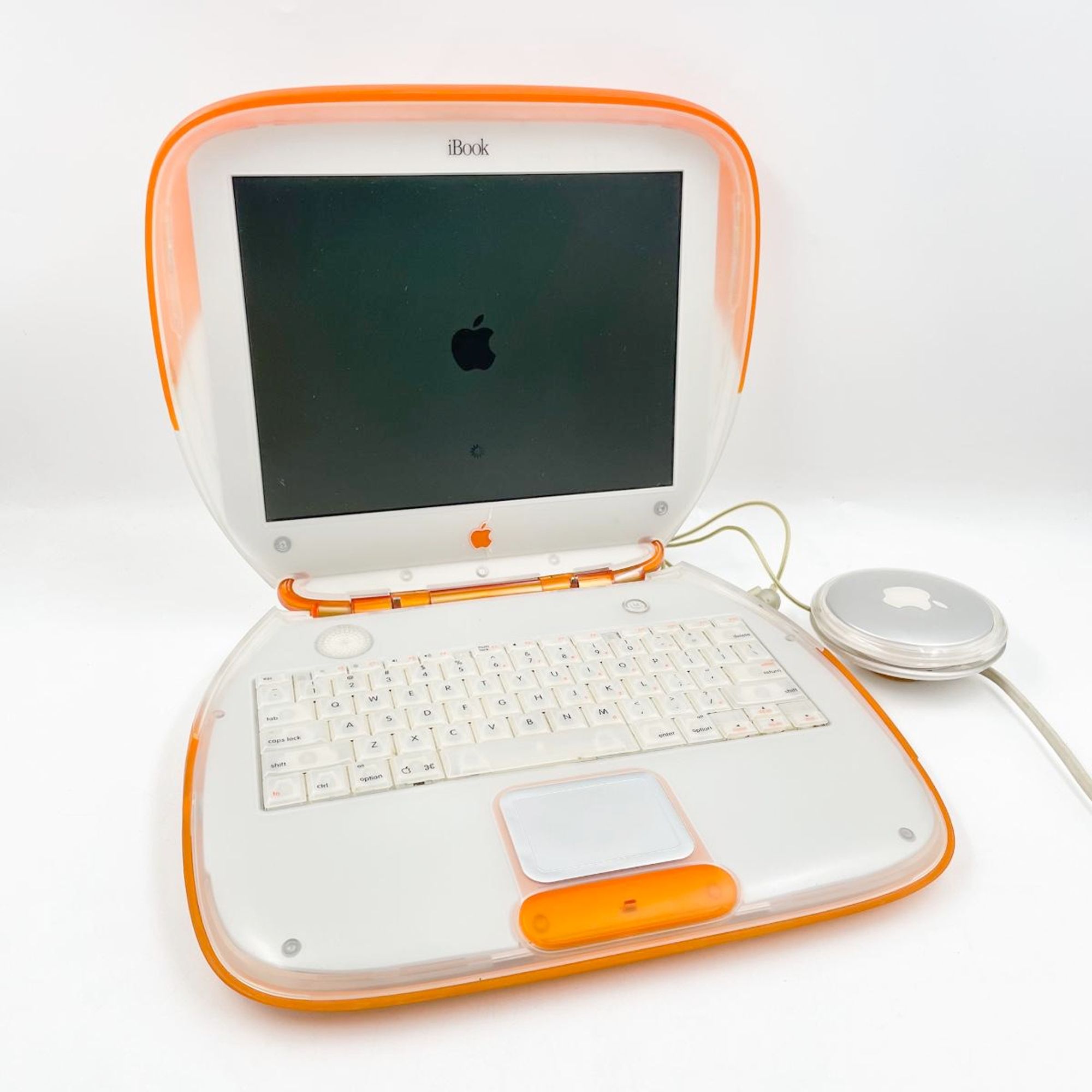 A tangerine clamshell iBook, opened, from an era when computer design was a bit more fun. Said wraparound power brick is off to one side, with the bitten apple logo.