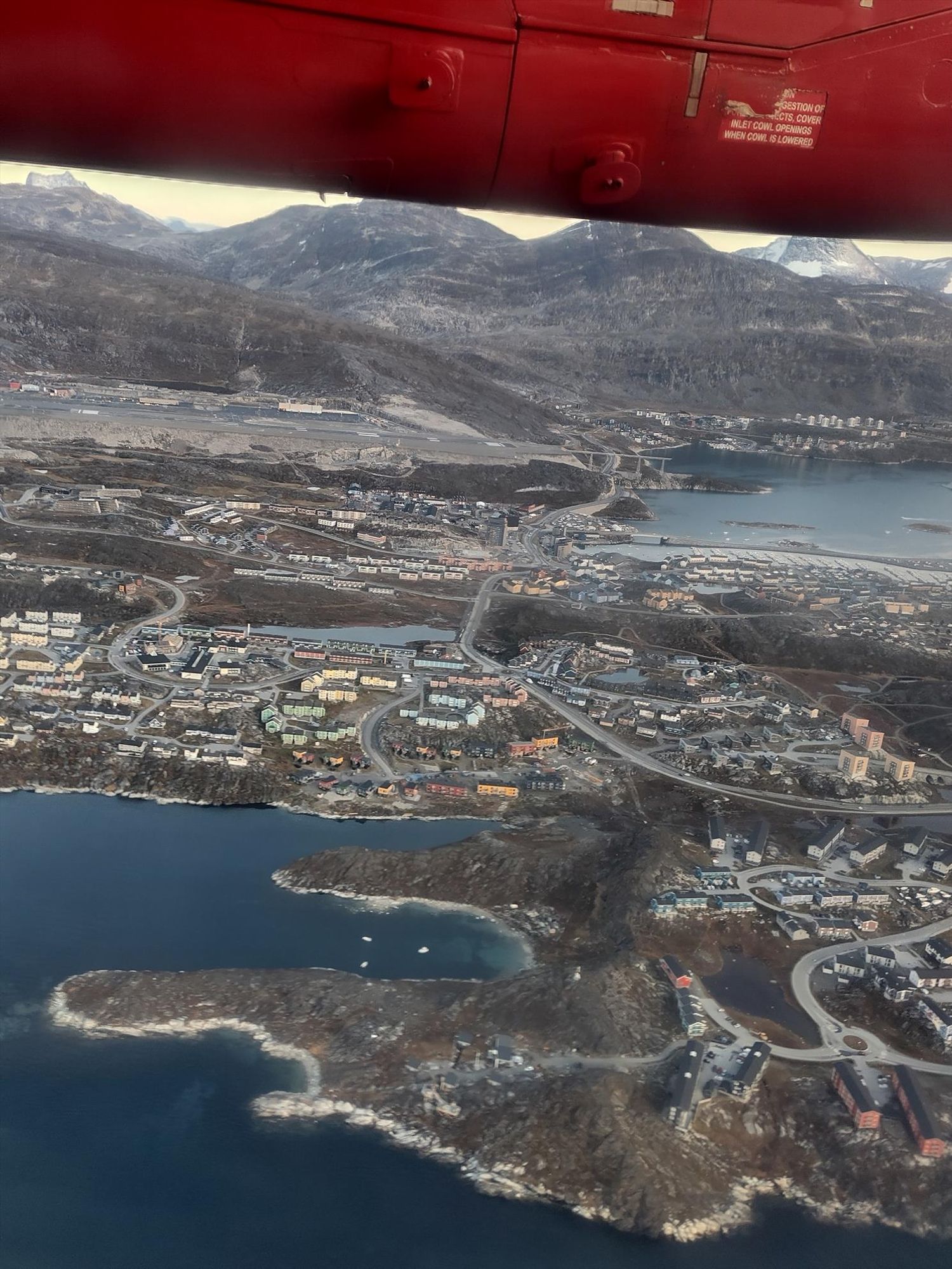 View from a plane window of a small town with colourful wooden houses next to the sea with a mountain in the background 