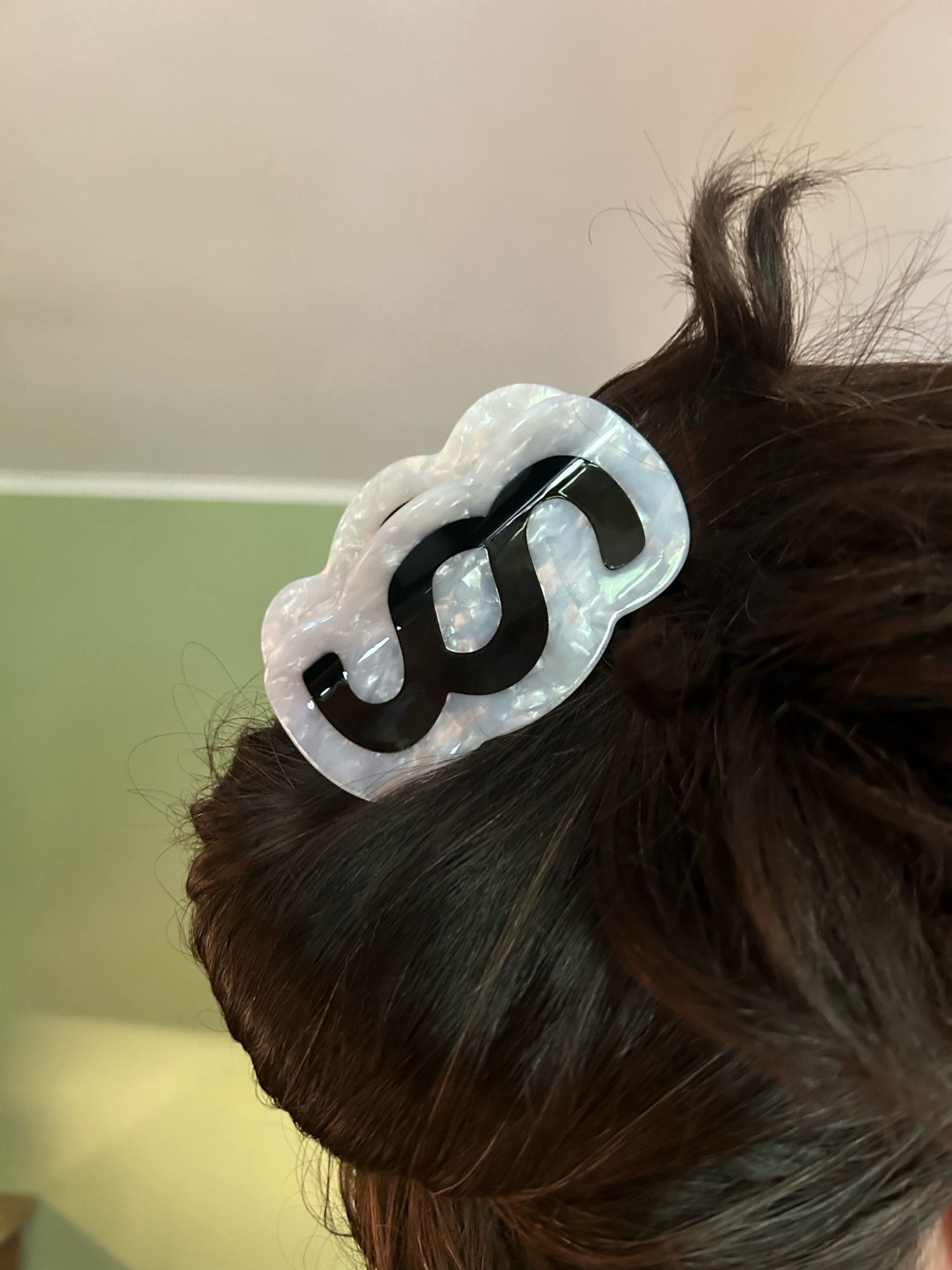 Photo of a white sparkly hair clip with the section symbol printed on it very large in bold black. It is holding up my dark brown hair very nicely.