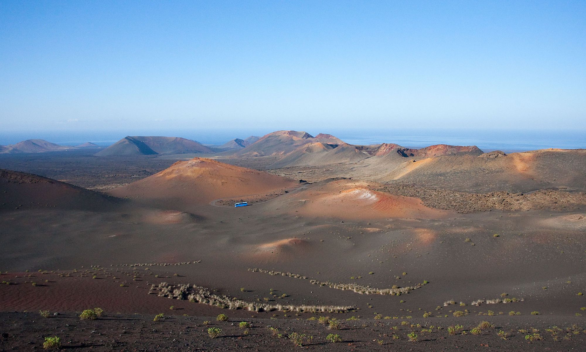 Ein Blick auf die Vulkanlandschaft im Nationalpark auf Lanzarote. Ein blauer Bus fährt in einer kargen Landschaft.