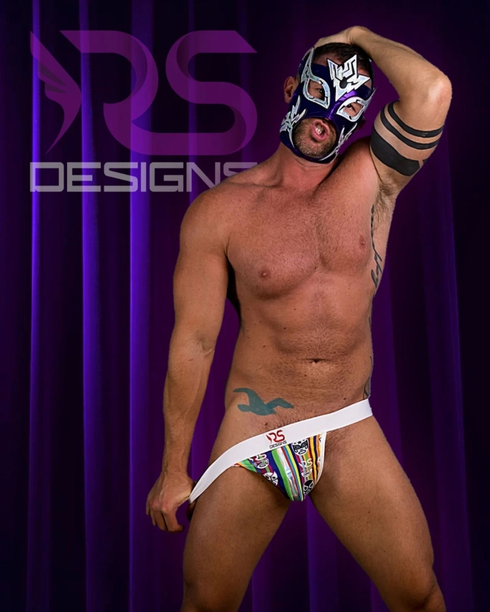 Masked very fit mail wrestler wearing a bright colored jockstrap with a laser stripe down the center of a Lucha Libre mask fabric created and designed by Raw Studio Designs. The model is tugging on the waistband as to imply taking it off.