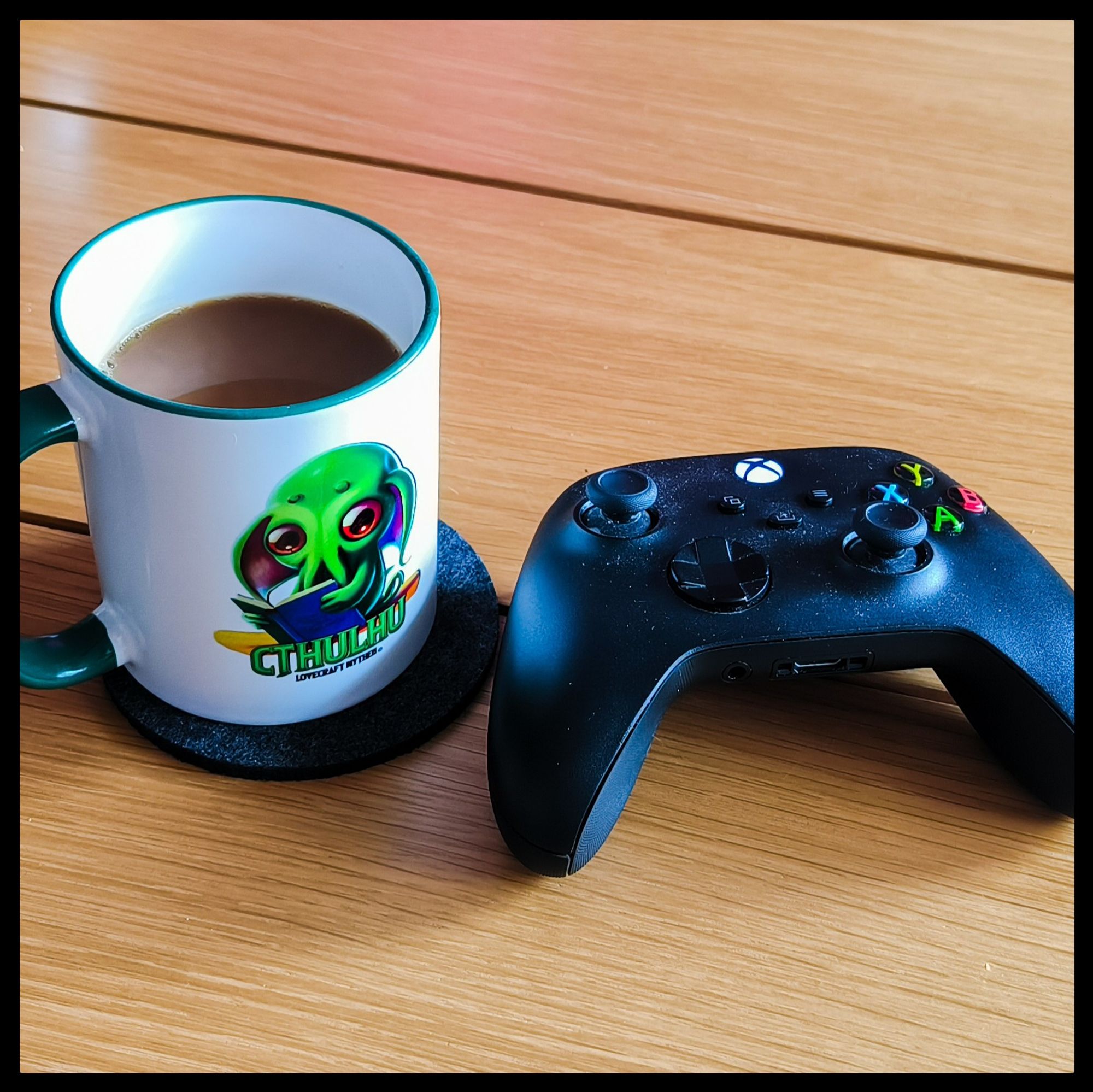 Eine Kaffeetasse und ein XBox-Controller nebeneinander auf einem Tisch.