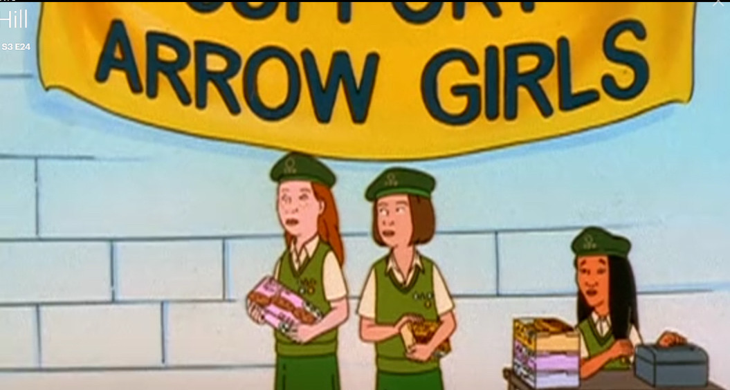 Screenshot of young Connie selling cookies with two other girls in scout uniforms and an “Arrow Girls” banner behind them