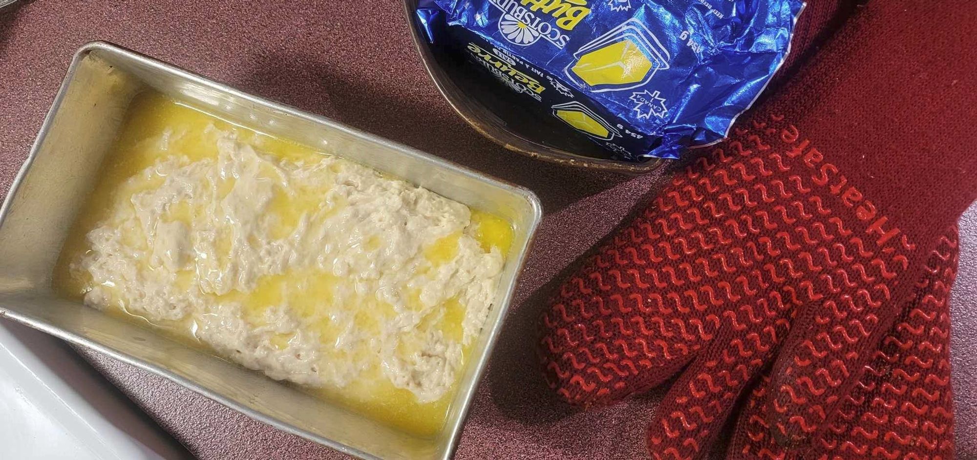 pan of uncooked bread next to oven mitts and butter.