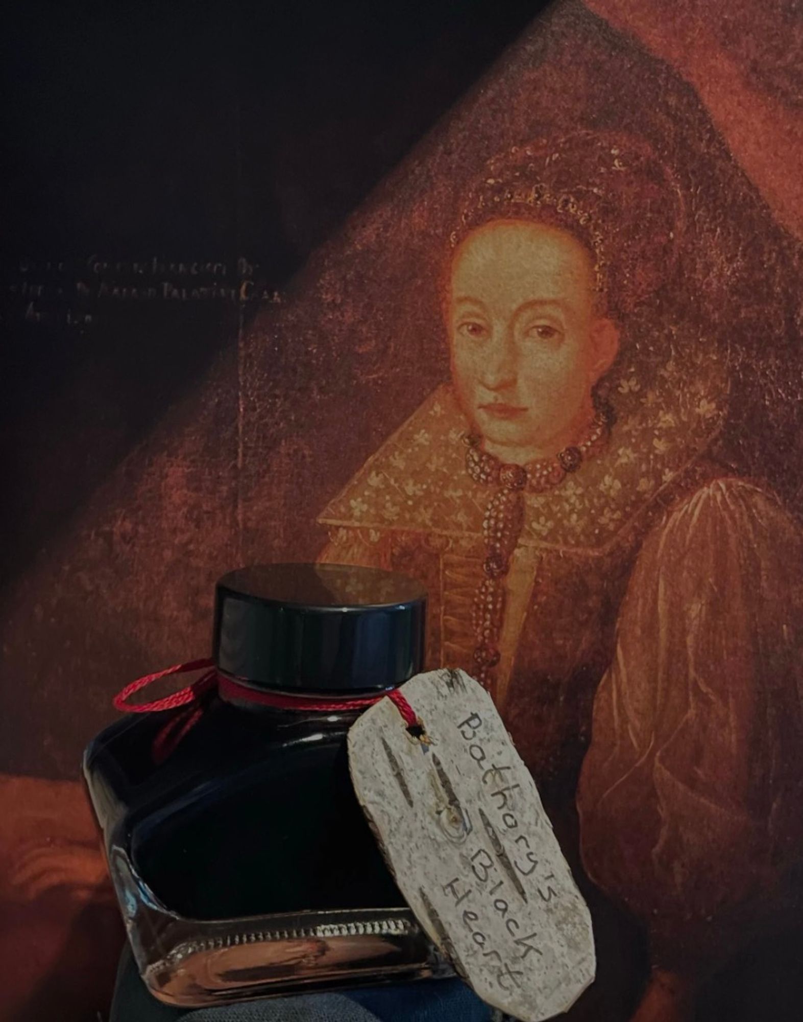 A small bottle of Bathory's Black Heart ink with a portrait of Erzebet Bathory as the background.