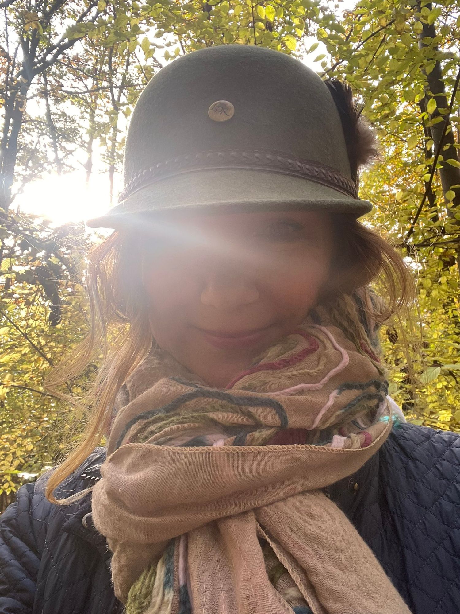 A picture of our Maker of Magical Natural Inks wearing a hat and scarf with sunlight shining from between the trees behind her.