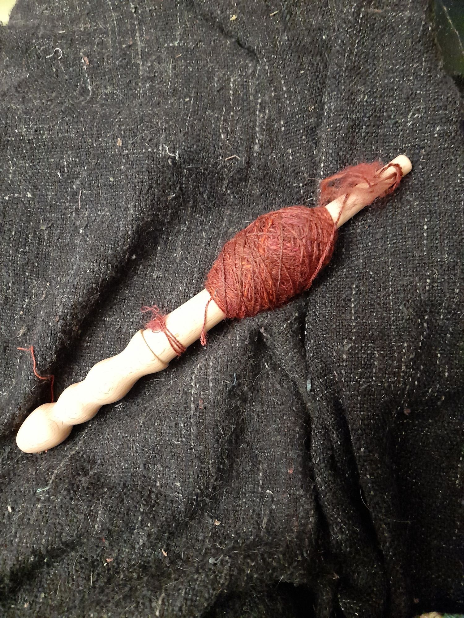 It's a wooden stick about 30cm long. One end is shaped to be a handle. The main shaft is slightly tapered. There's thin variegated red yarn wrapped in a criss cross pattern into a ball around the shaft.