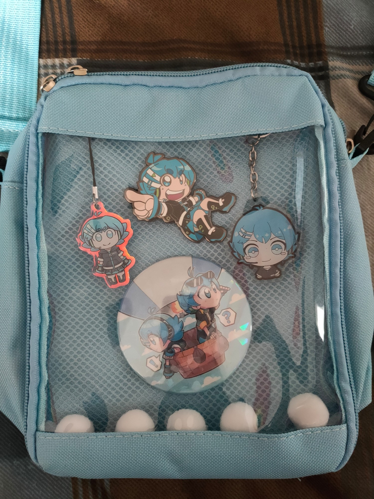 Small light blue Ita bag featuring Kikyuune Aiko. Inside is 5 white pom pom balls, a large badge featuring Utau and Mikoto Studio Aiko in a hot air balloon, a small Aiko keychain, a Chibi bust keyring and an Aiko pin. All merch is from MystSaphyr except for the keyring which is by Untamen_Taro