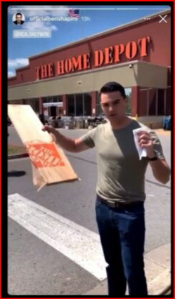 Ben Shapiro looking like an idiot in front of Home Depot holding a piece of wood in a too-small paper bag.