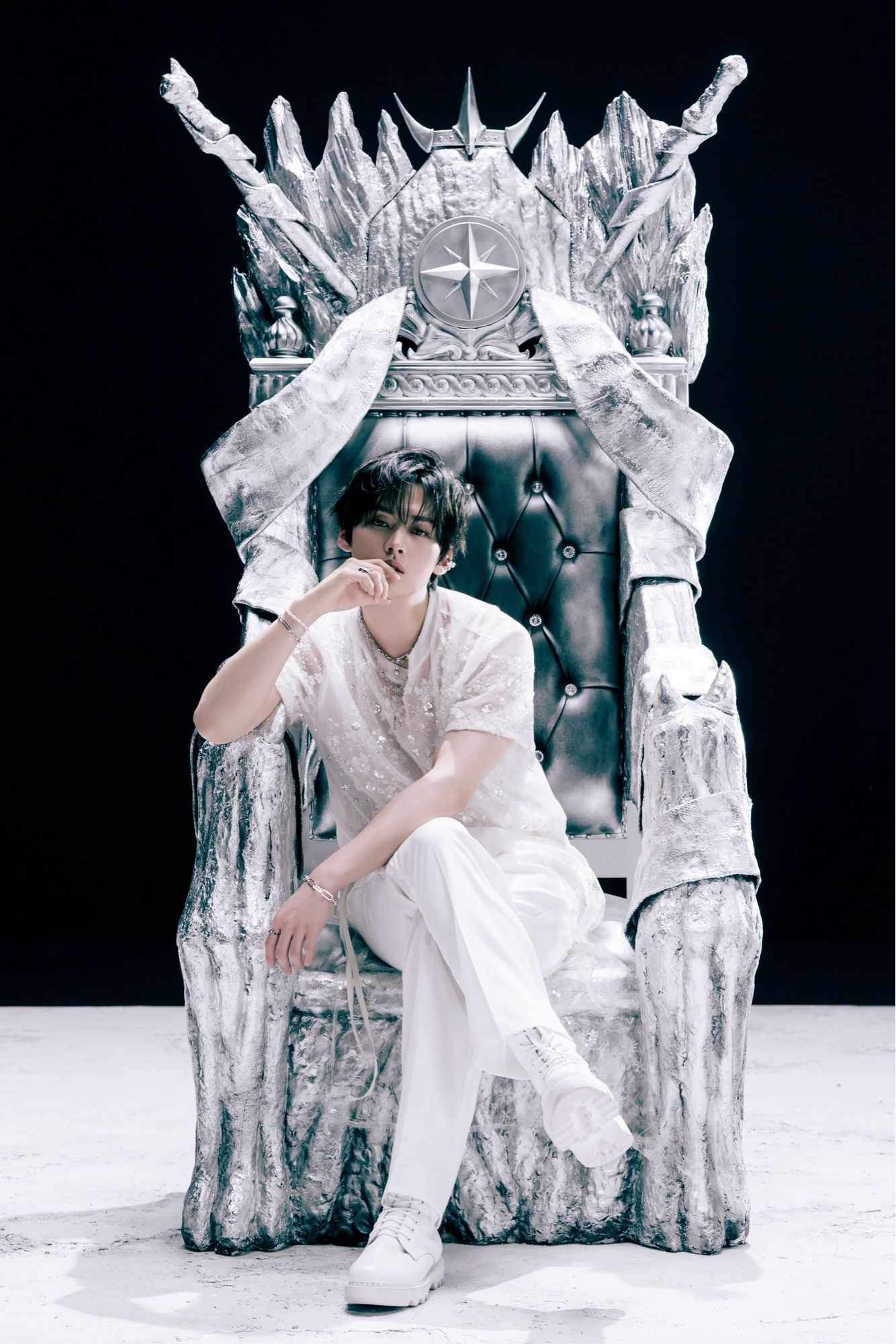 Lee Know dressed in all white sitting on a silver looking throne.