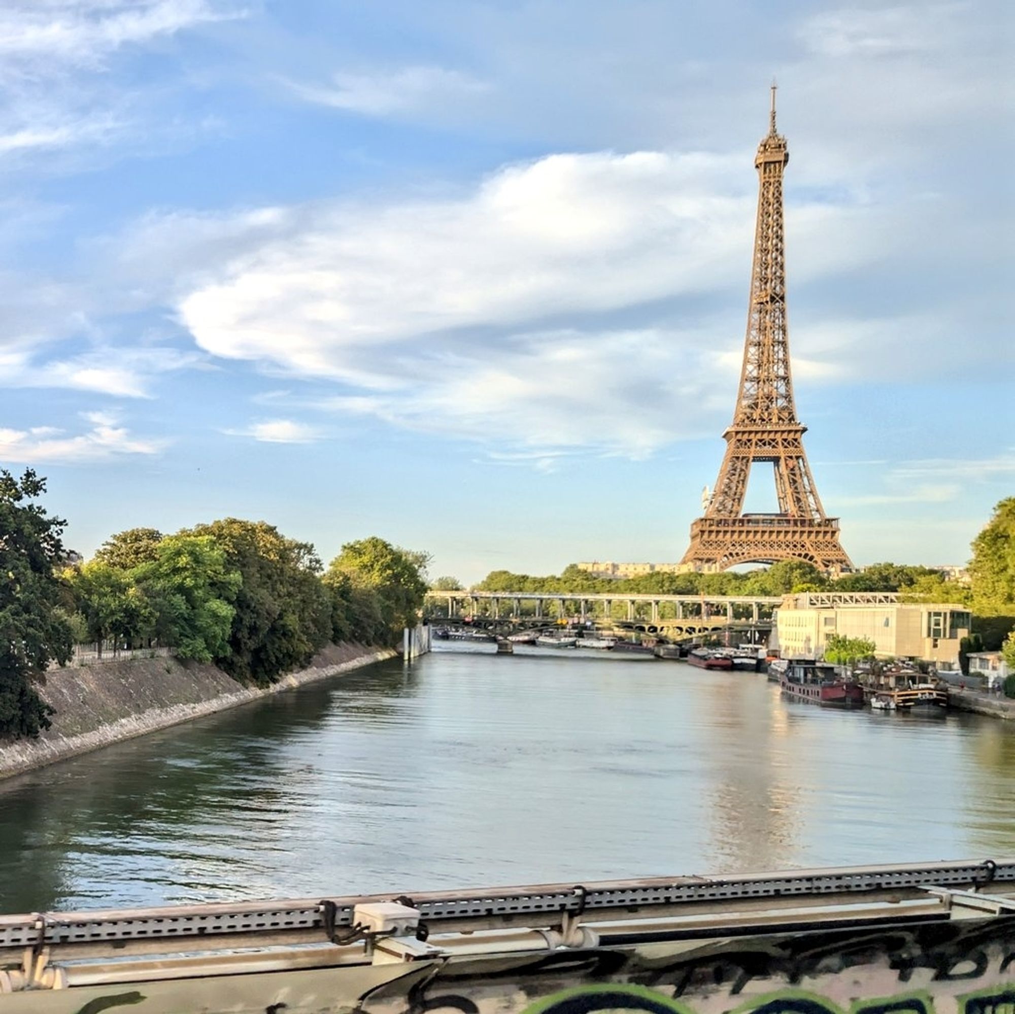 Vue sur la Seine et la Tour Eiffel depuis le viaduc du RER C, sur un ciel bleu légèrement voilé.