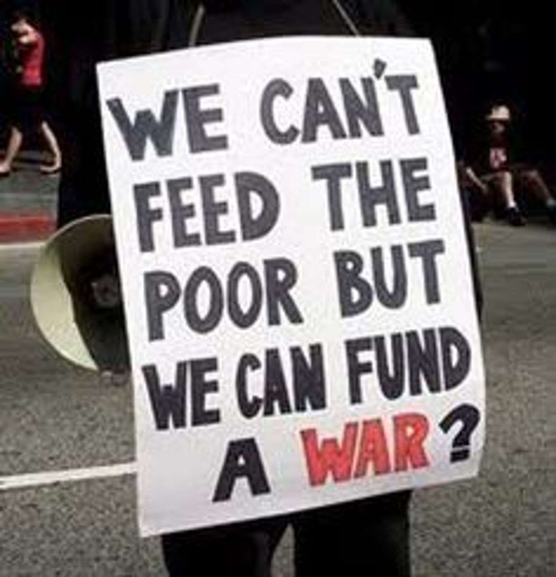 A protester holding a sign that reads, "We can't feed the poor but we can fund a war".