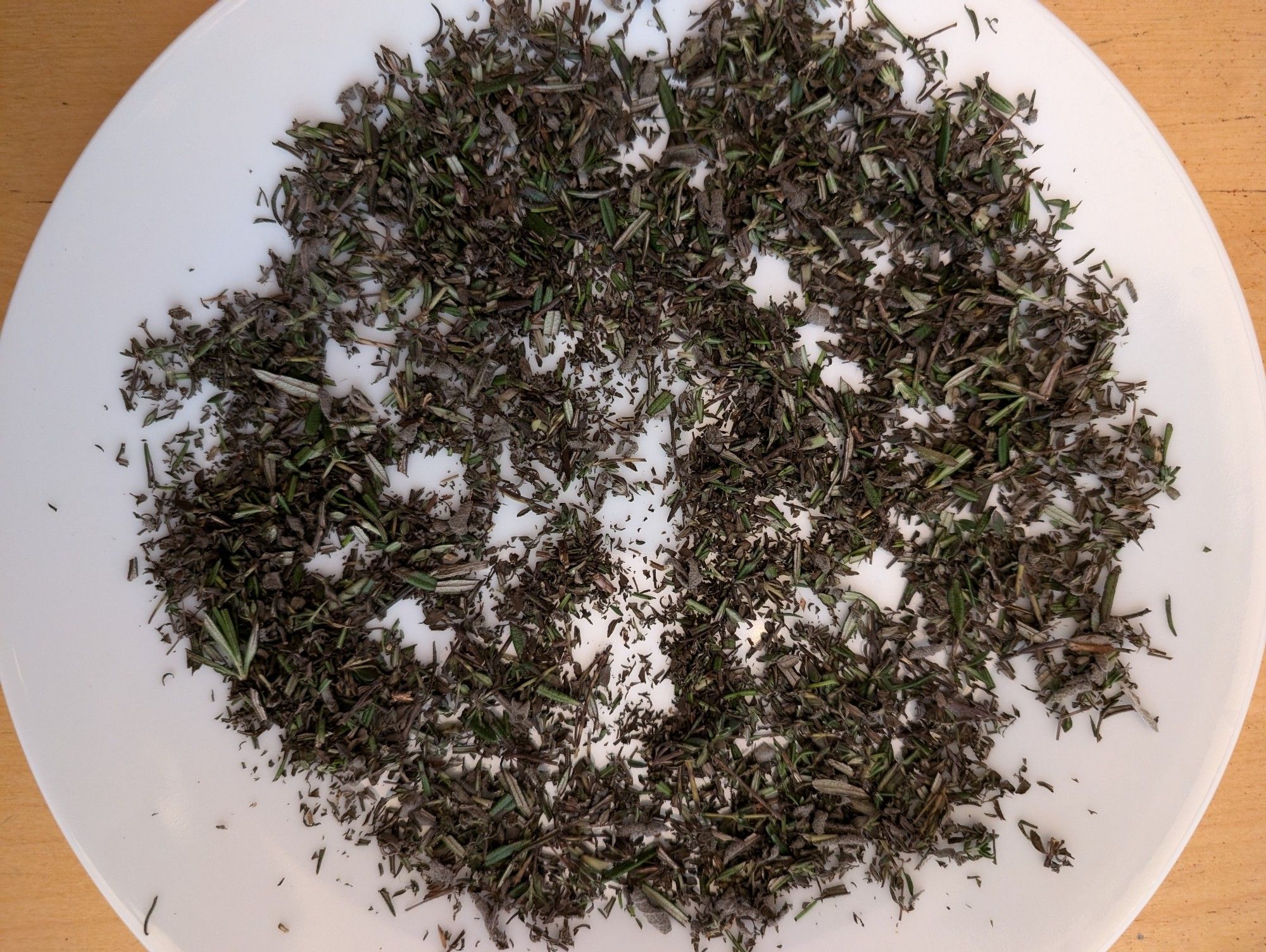 Chopped thyme, sage and rosemary on a plate.