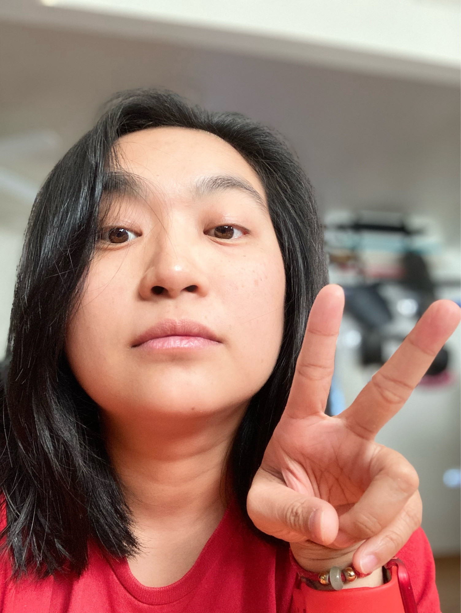 selfies of nonbinary Asian person doing peace sign, indoors with good lighting, no glasses, red T-shirt