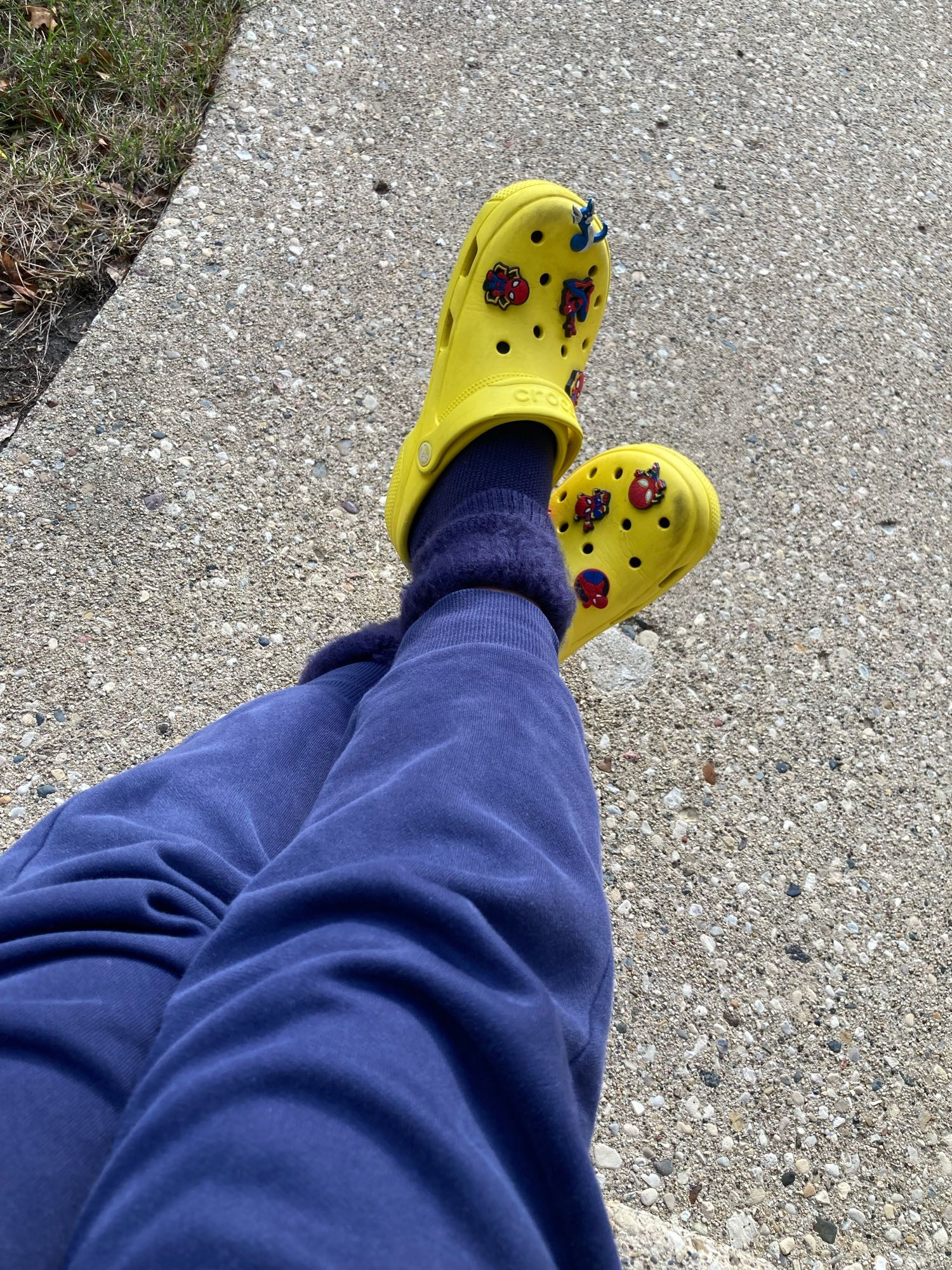 Photo of legs wearing navy sweatpants, navy fluffy socks, and bright yellow Crocs with spider-man charms