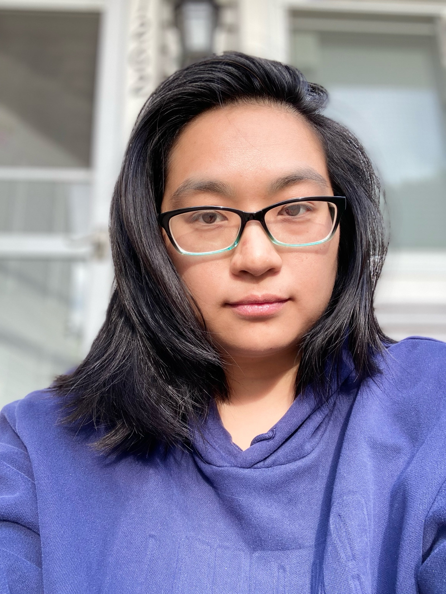 Photos of Asian nonbinary person with glasses on wearing a navy sweat suit combo sitting outside in front of a house 
