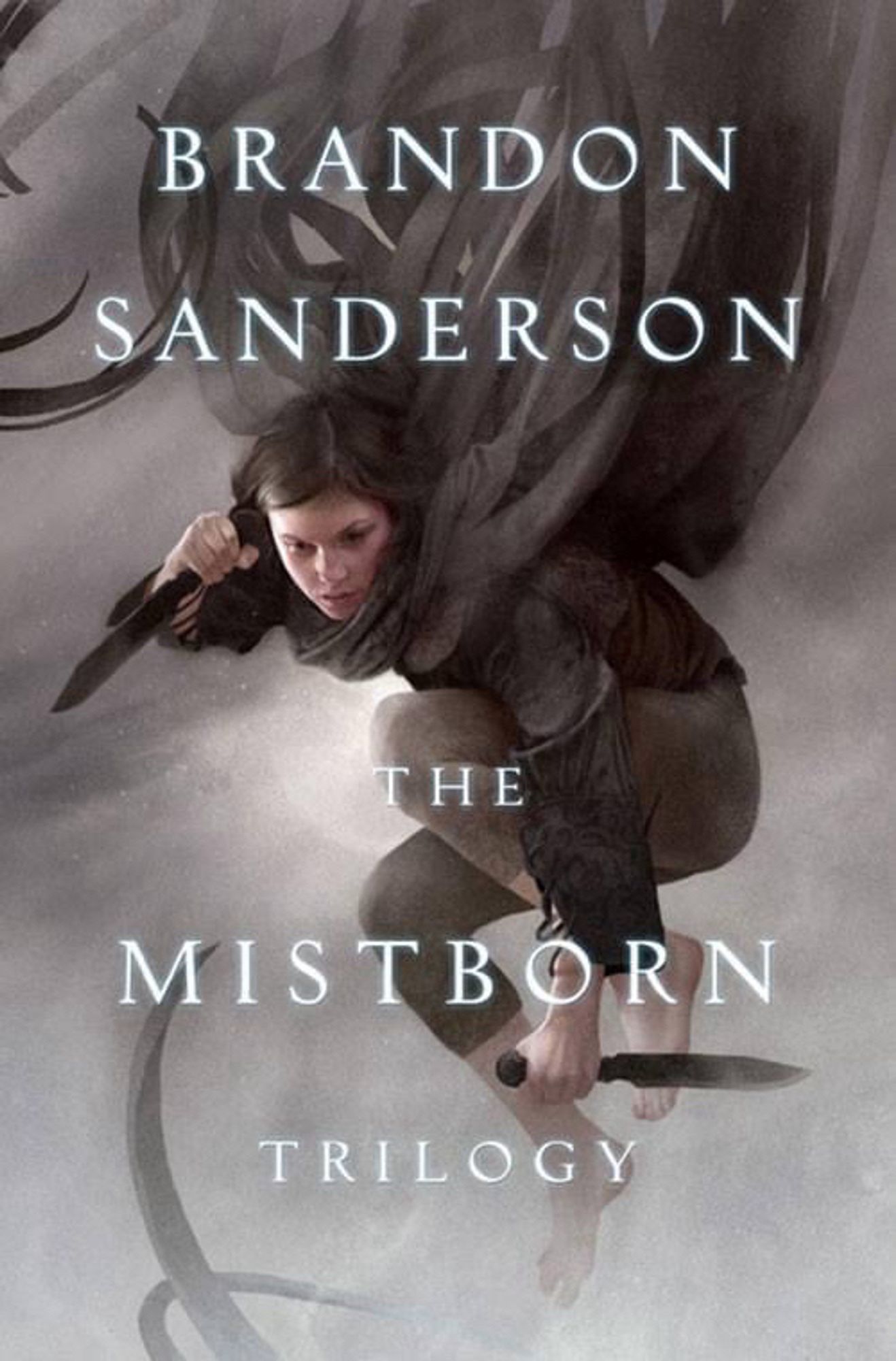 A girl leaping in midair holding two daggers, wearing a cloak made of think strips of fabric trailing behind her back. Top: “Brandon Sanderson” Bottom: “The Mistborn Trilogy”