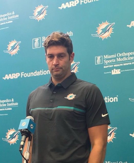 Jay Cutler (nfl quarterback who does not particularly like playing football) at a Miami dolphins press conference, looking down, pondering the choices in life that led him to this foresaken moment