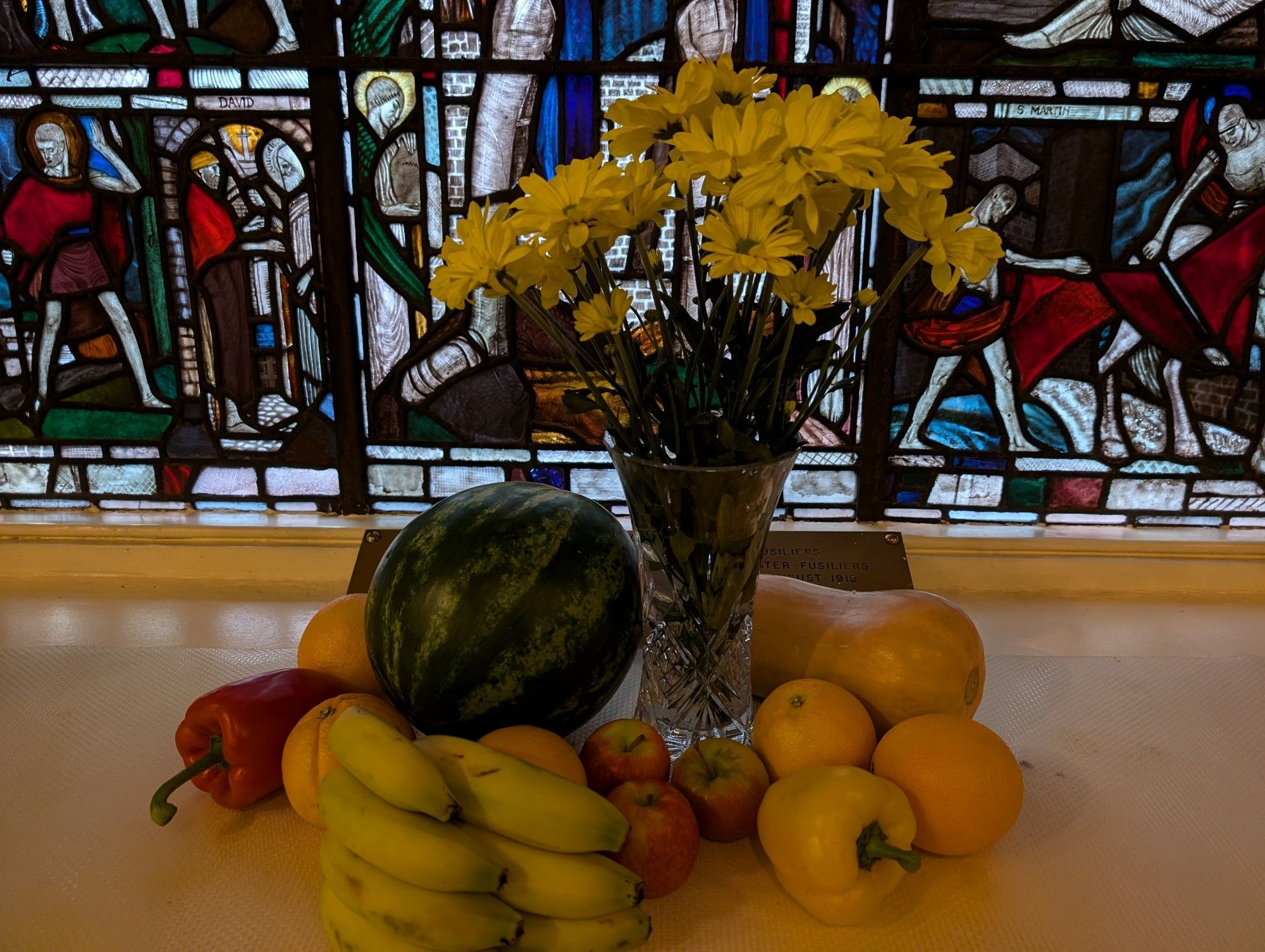 Fruit and a vase of flowers in front of a stained glass window