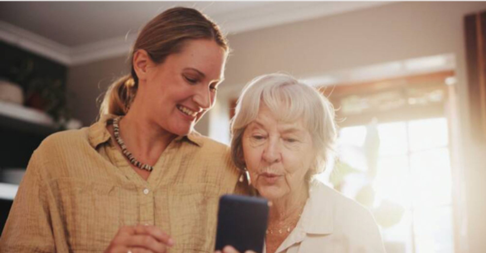 2 women standing together smiling looking at a mobile phone screen