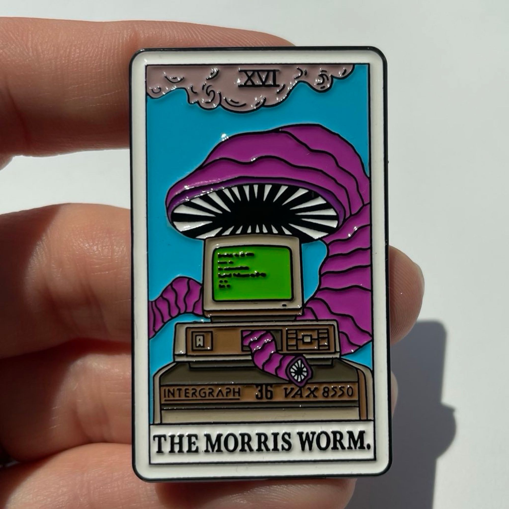 Image is of an enamel pin depicting a worm eating a computer. It’s in the style of a tarot card and has the words “the morris worm” at the bottom.