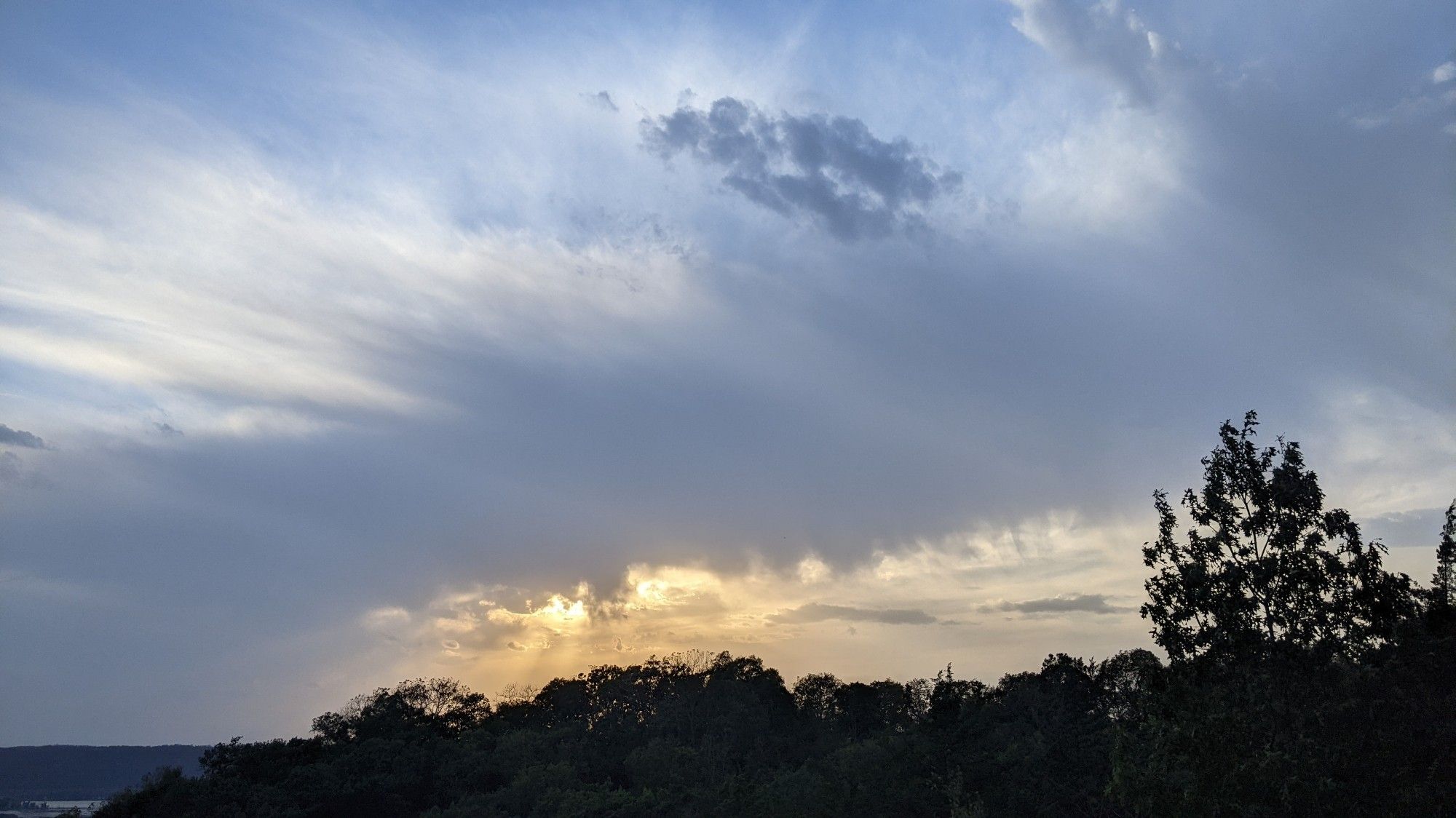 Looking west, sun obscured by band of clouds. Gold and peach colors underneath, and blue, white over the top