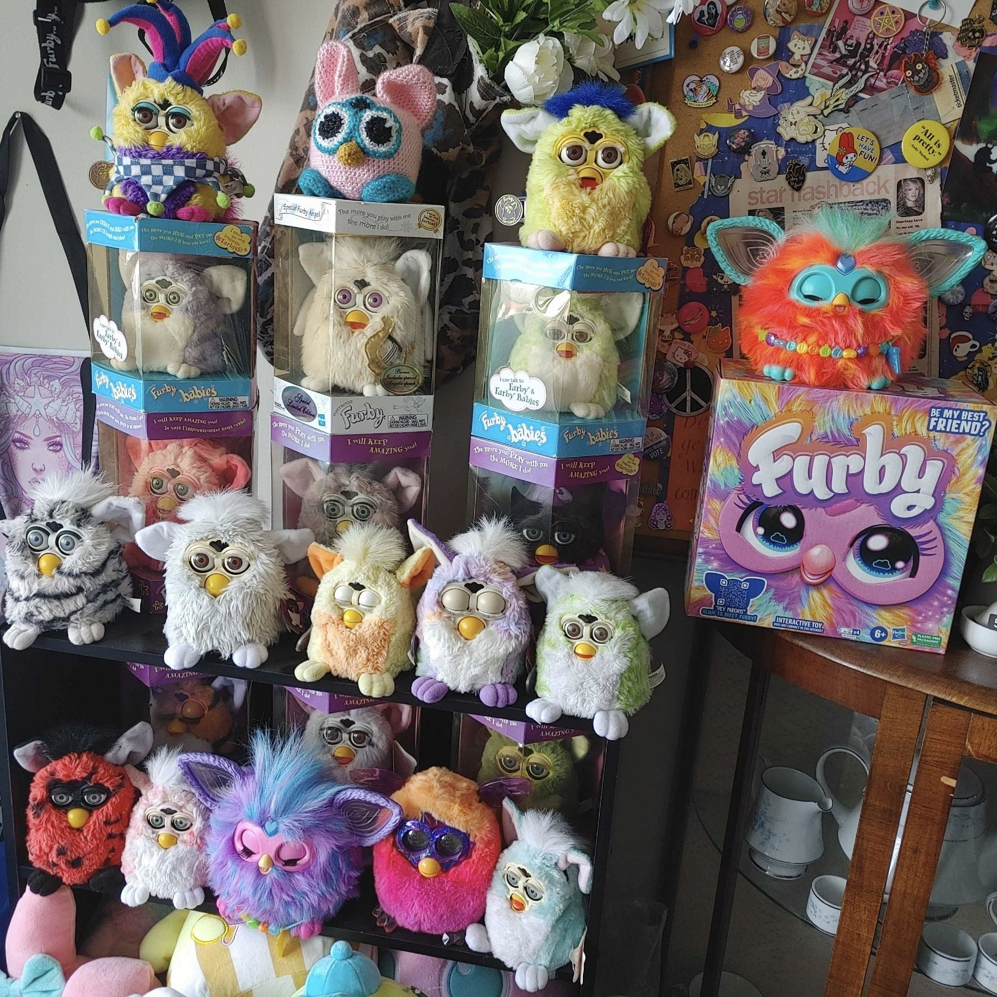 Roxi's vintage furby collection from left to right, top to bottom: 1998 Jester Furby unboxed, a one of a kind crochet furby made by a friend of Roxi's that was a gift, a 1998 Kiwi Lime Furby unboxed, unboxed orange 2023 Furby on top of a box for a 2023 Rainbow Furby with furby inside but unviewable, 1999 purple Furby baby in box, limited edition 1998 Angel Furby in box, 1999 Lime Furby baby in box, pink 1998 Furby in box, wolf 1998 Furby in box, 1998 wizard Furby in box, zebra/striped Furby 1998 unboxed, champagne Furby 1998 unboxed, yellow Furby baby 1999 unboxed, tie dye 1998 Furby unboxed, lime Furby baby 1999 unboxed, tiger furby 1998 in box, leopard furby 1998 in box, frog furby 1998 in box, lady bug 1998 furby unboxed, 1999 coral furby baby unboxed, purple 2023 furby unboxed, orange pink Furby crystal boom 2015, mint 1999 furby baby unboxed