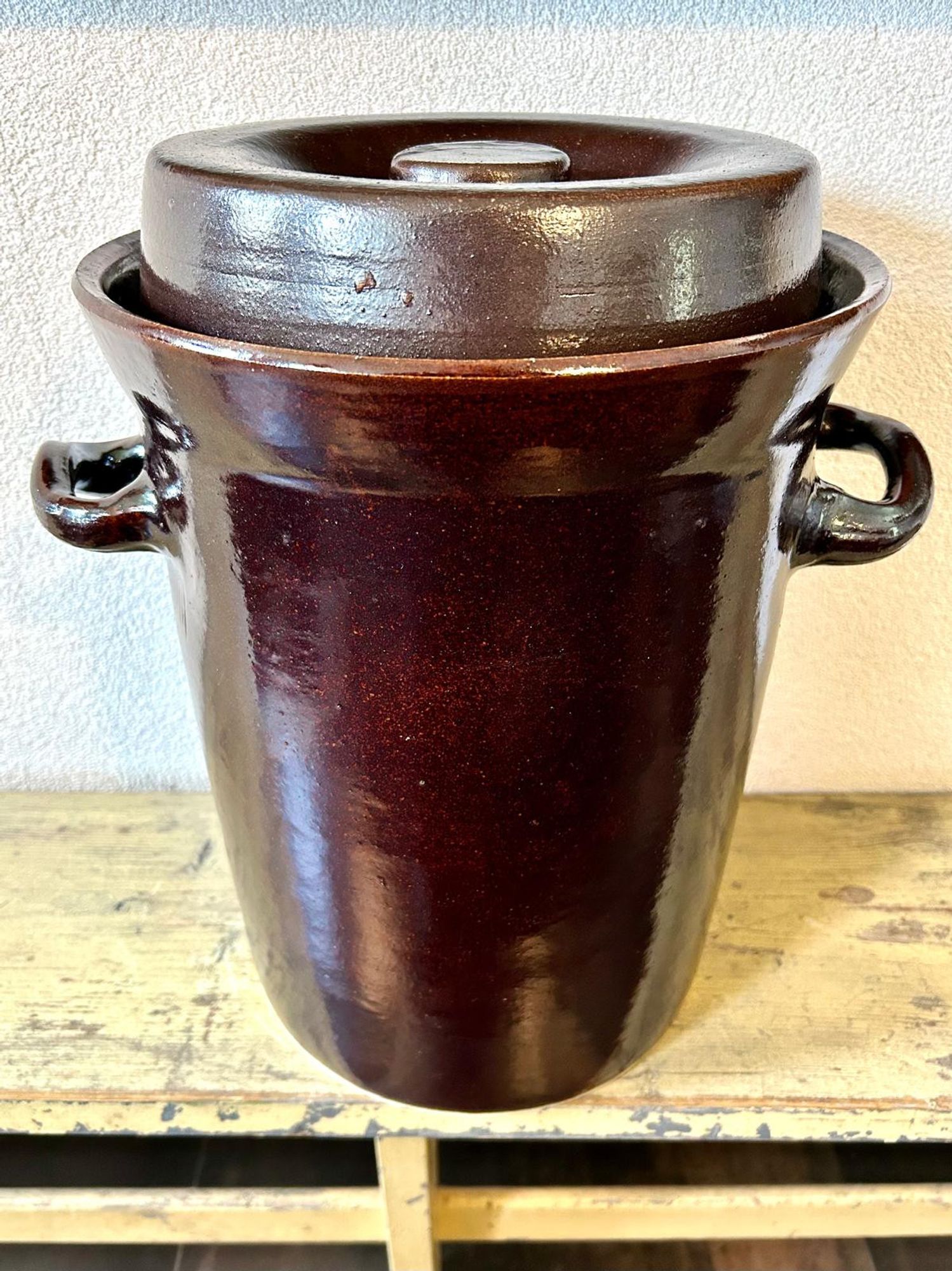 An earthware sauerkraut pot with lid on. Sitting on an old school bench in our kitchen.