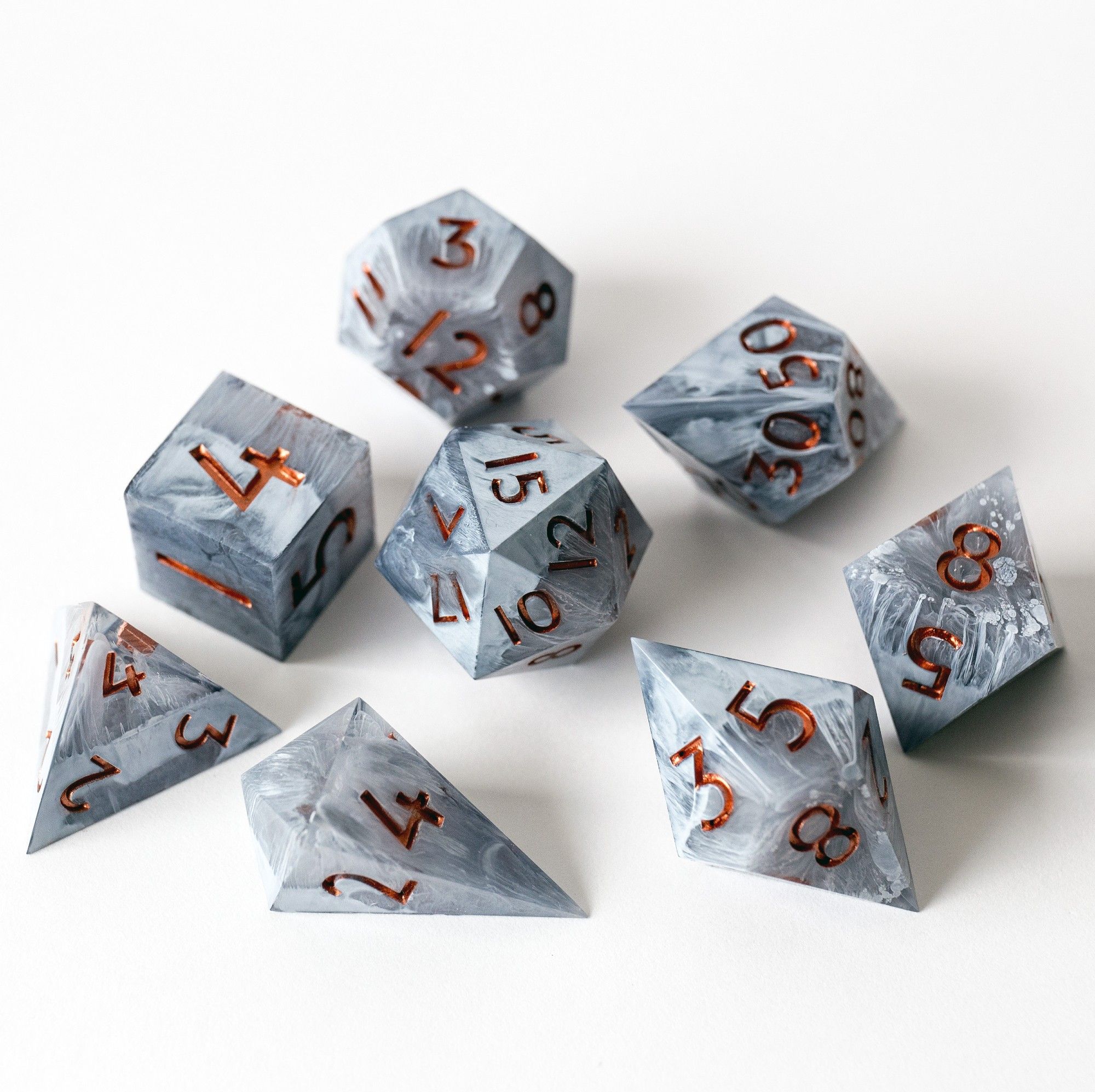 Ein weiteres Bild vom kompletten Set. Alle Würfel sind gut zu erkennen und liegen verstreut auf einem weißen Untergrund. Gut zu erkennen sind die weißen Verwirbelungen und der Marmor Effekt. Das Set besteht aus D4 Shard, D4 Pyramide, D6, D8, D10, D00, D12 und D20.