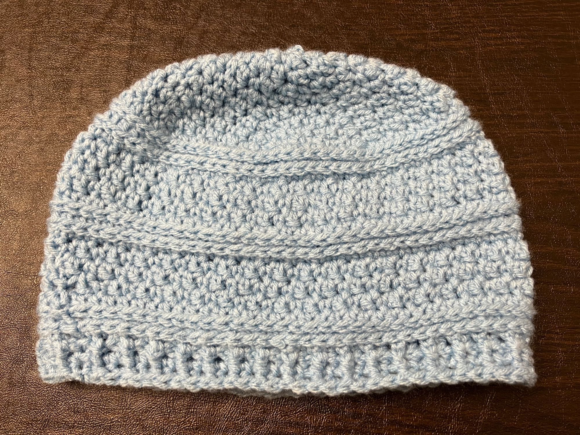 a photo of one hat crocheted from light blue yarn on a dark background