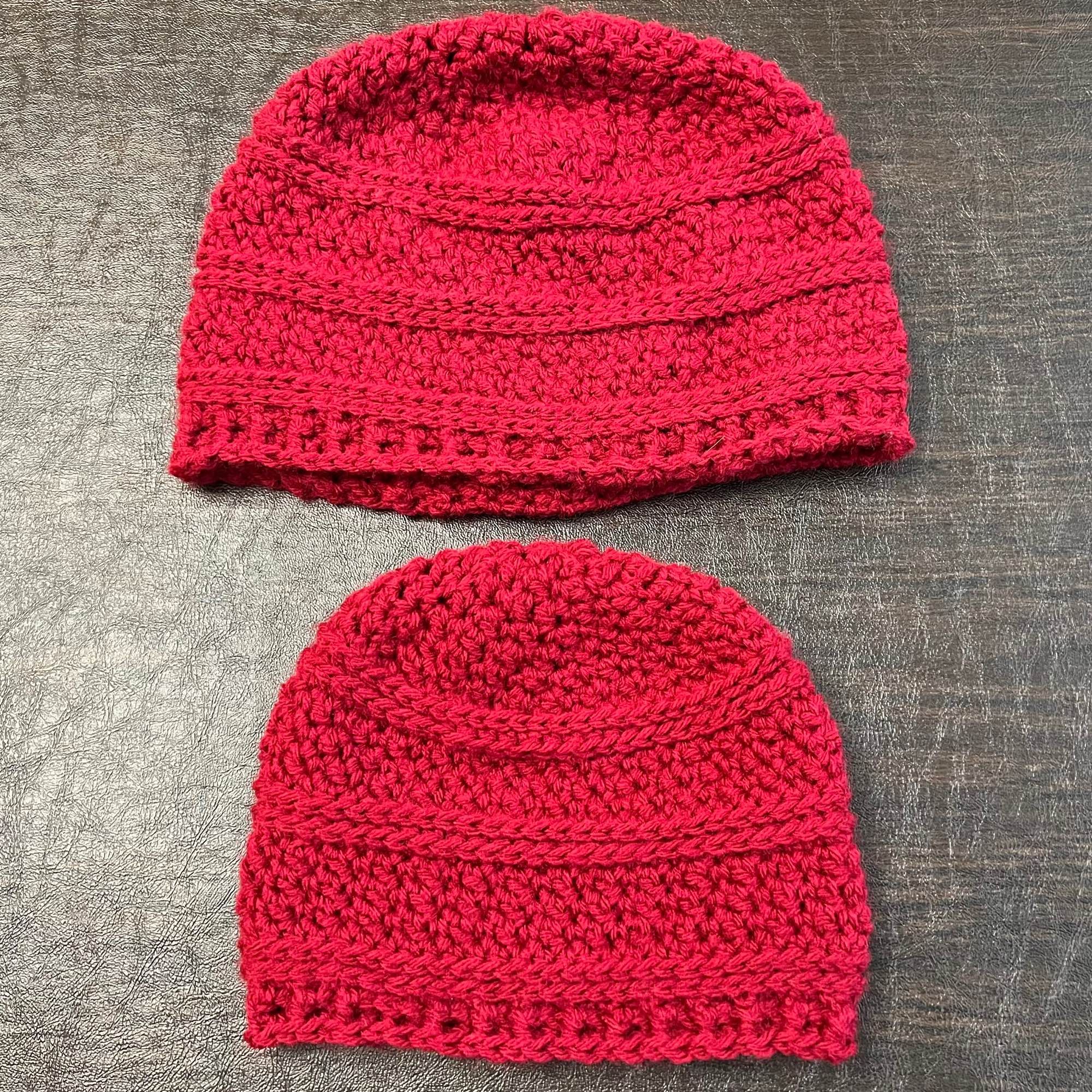 a photo of two hats crocheted from red yarn on a dark background