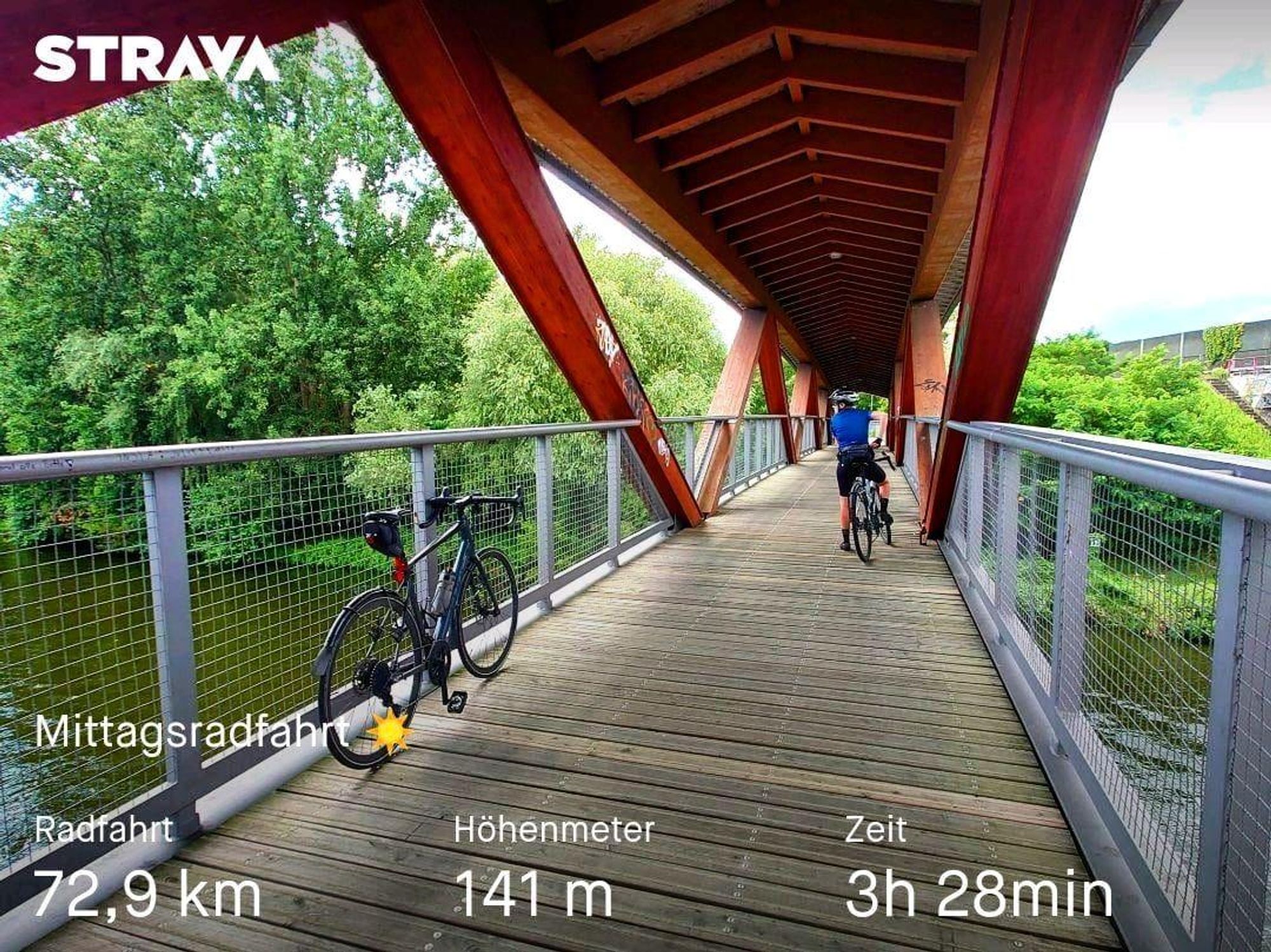 Auf einer Brücke steht links am Geländer ein Rennrad, etwas weiter hinten eine Person mit Gravelbike. Die Brücke hat einen Holzboden und ein rotes Holzdach. Die Geländer sind aus Metall. 