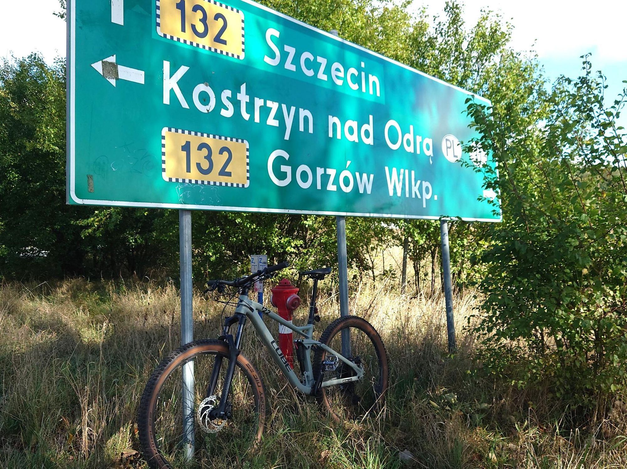 Ein graues Fahrrad steht vor einem Straßenwegweiser. Der Wegweiser zeigt die Richtung nach Szczecin, Kostrzyn nad Odra und Grozow Wlkp an.