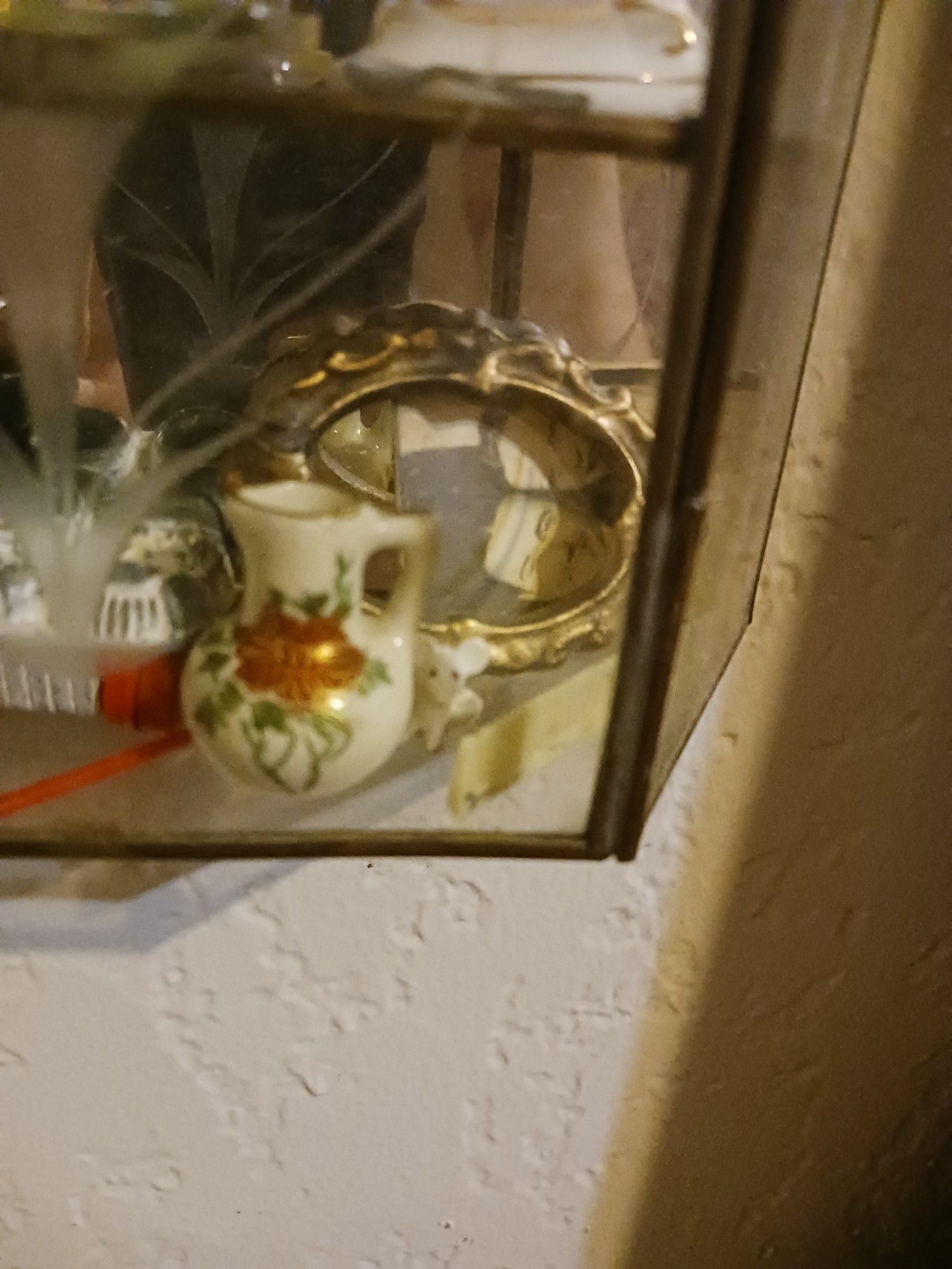 Close up on one corner of the brass and glass shelf, with a tiny mouse behind a dolls comb and in front of a tiny ornate vase. A photo of a 1920s couple rests sideways behind an oak Dollhouse frame