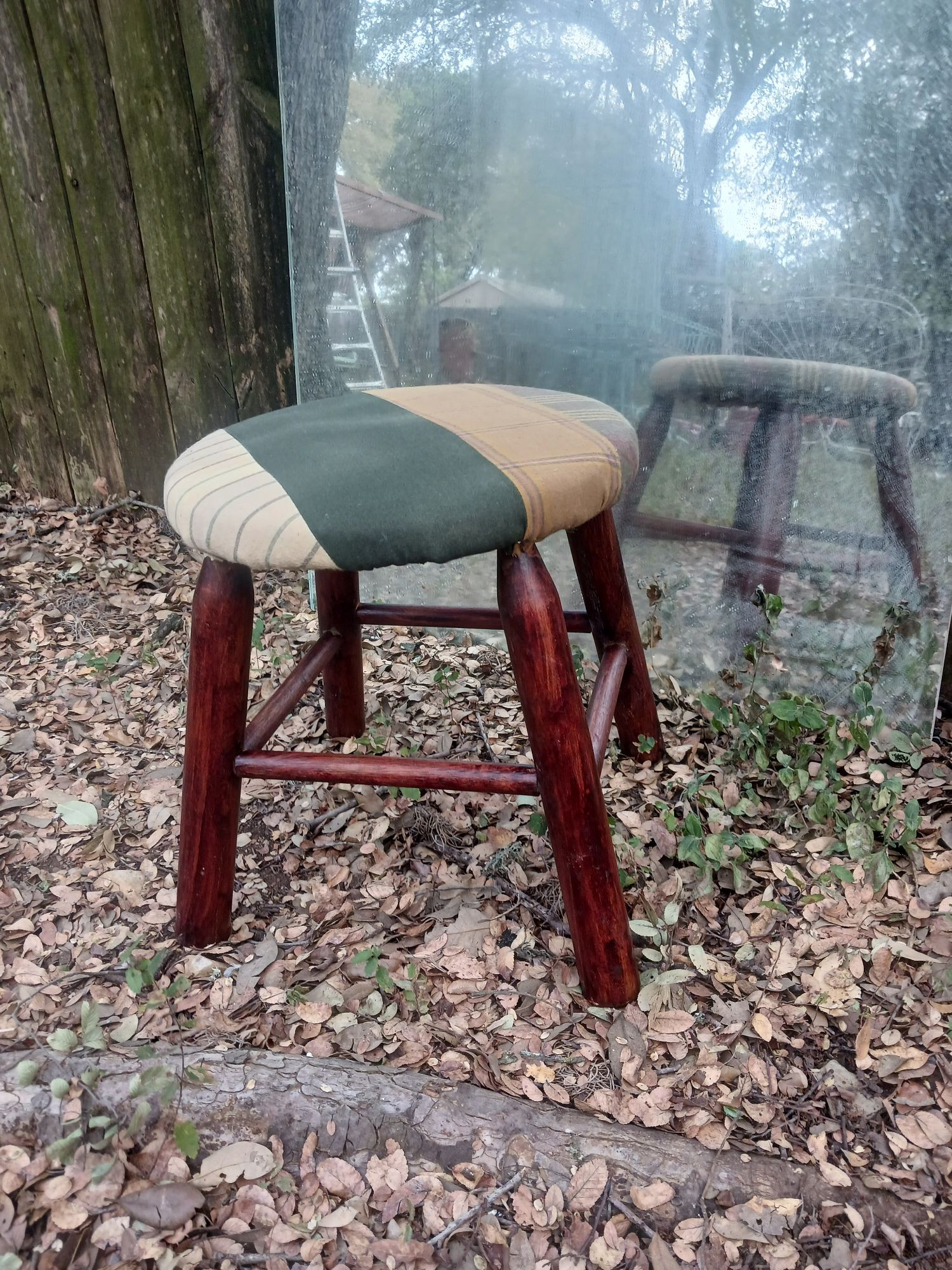 A dark wood stained round still upholstered in 4" stripes of green and tan flannel suiting, also outside in front of my mirror fence