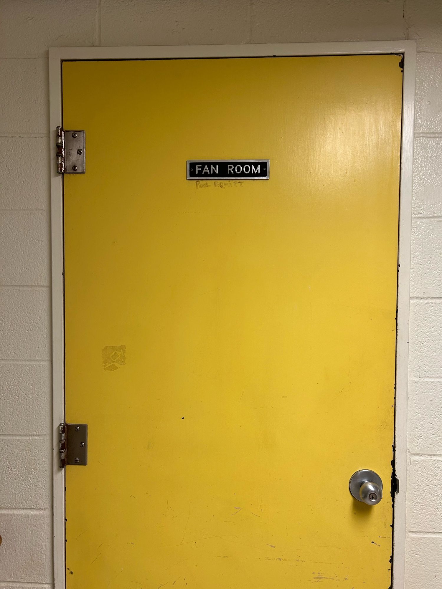 Big yellow door with a metal name plate that reads, “FAN ROOM”.