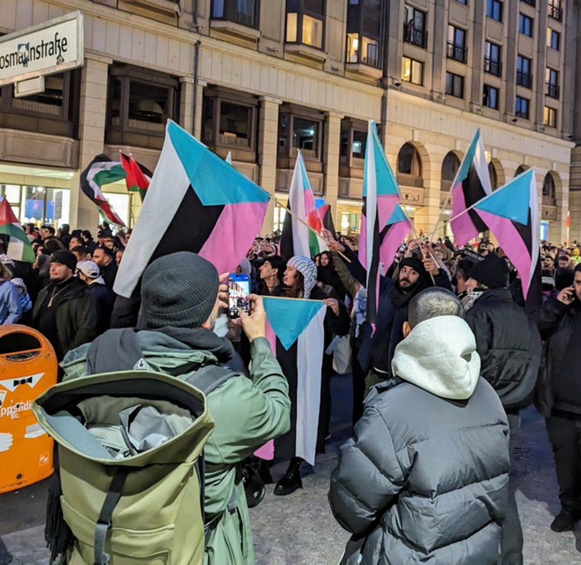 Eine Demo wo Flaggen der palistinänser in den Farben Weiß Schatz rosa blau gezeigt werden