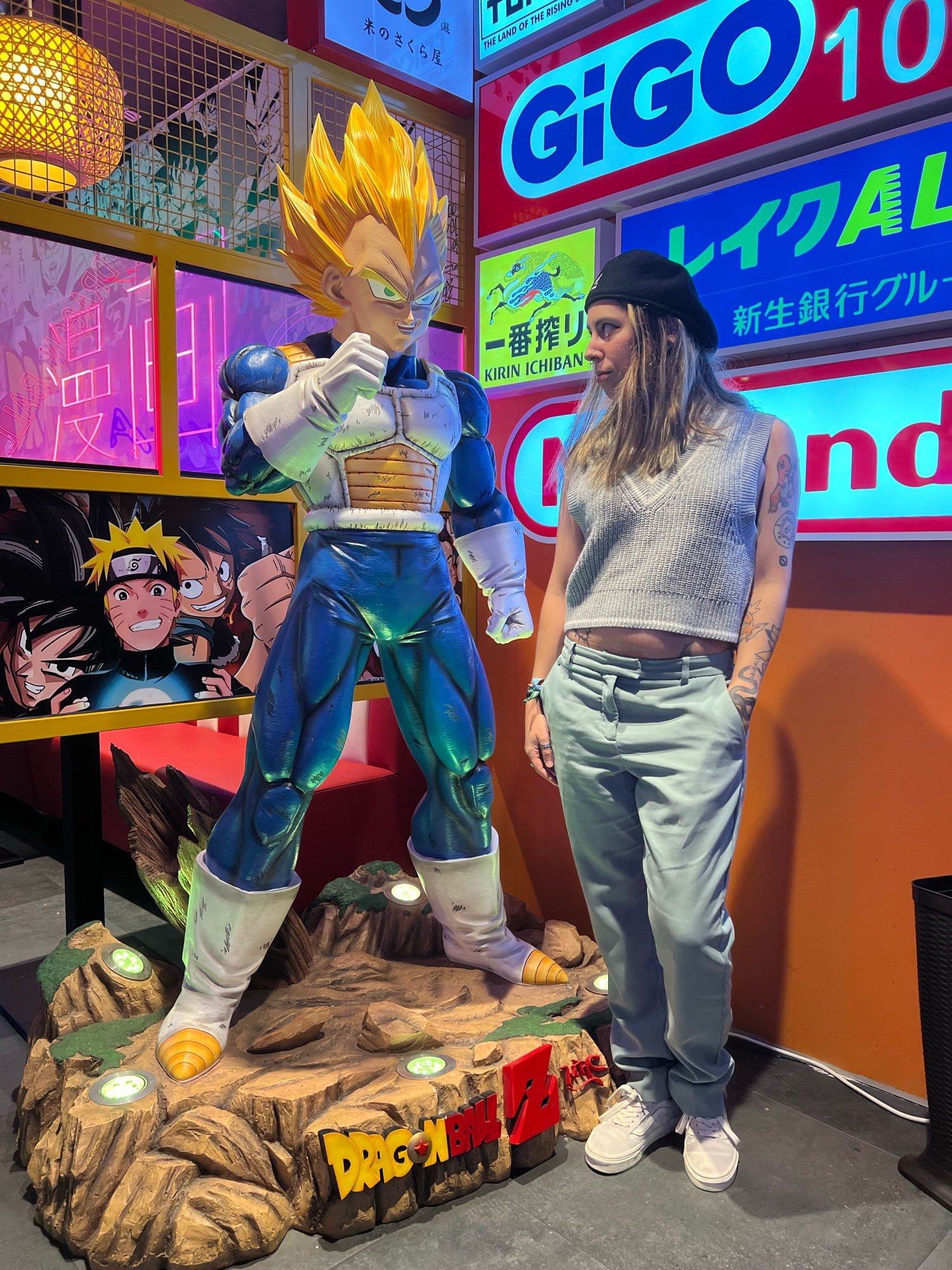 Yo con figura de Vegeta Súper Sayan de Dragon Ball Z en un local con muchos carteles luminosos