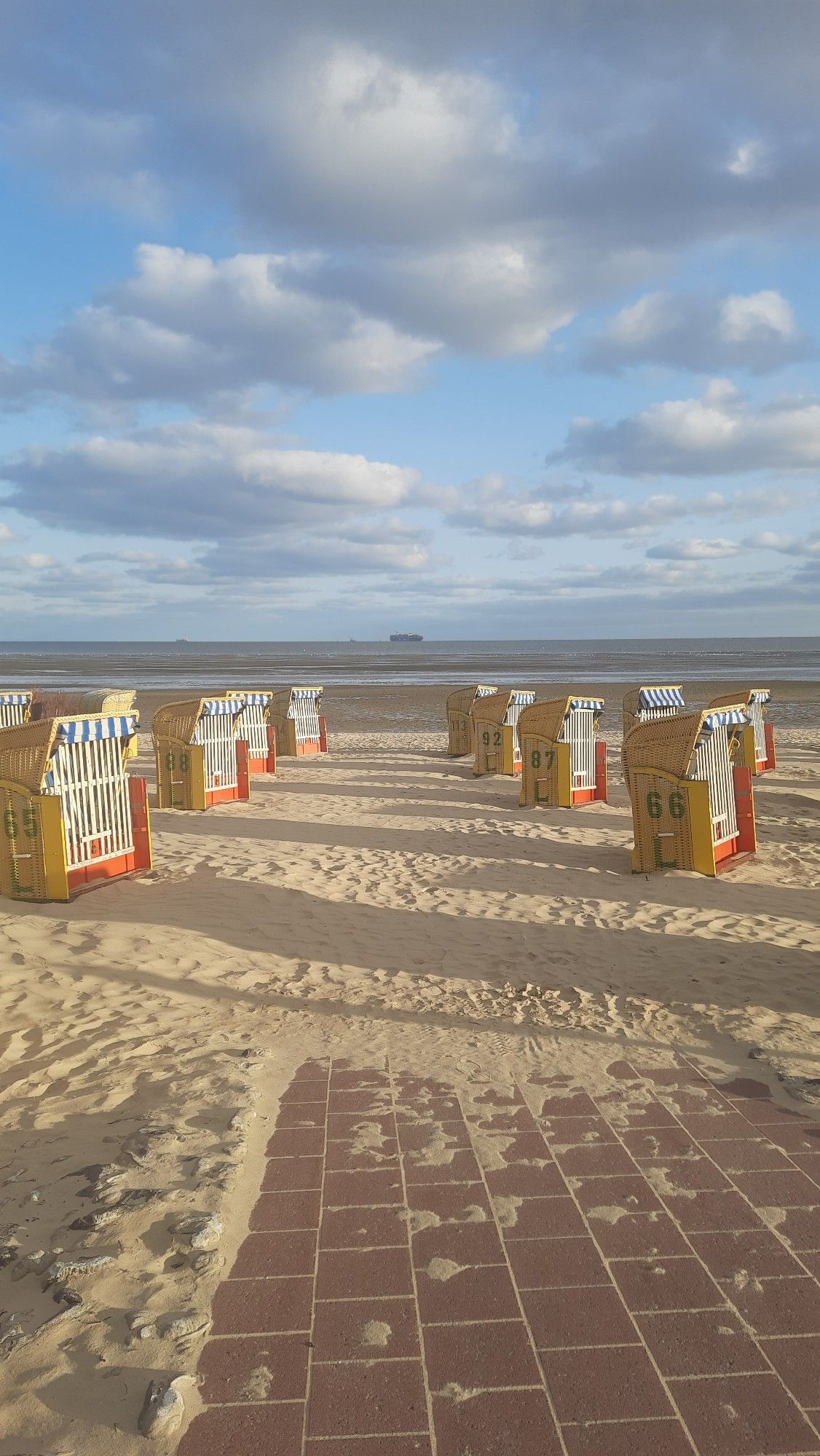 Blick am Strand Richtung Meer - zwischen Strandkörben hindurch ist ein Containerschiff zu erkennen.