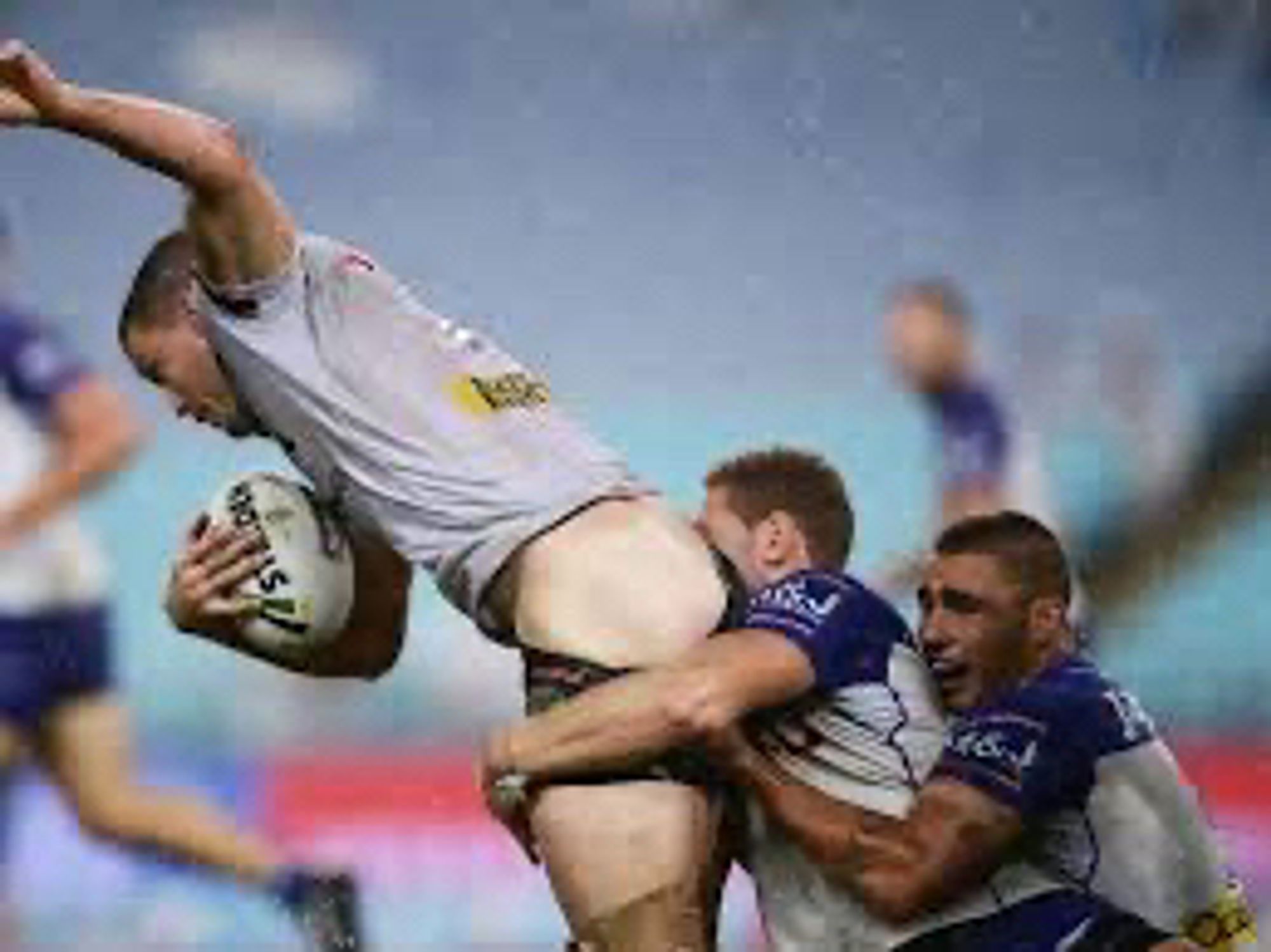 A picture of three rugbyplayers. First has the „ball“ or whatever this thing‘s called and tries to get away with one other sitting in his back trying to hold the first and burying his face deep in the buttocks of the first who’s shorts have slipped down somehow. The third player hugs the second sitting behind him and looking  anxious in a way