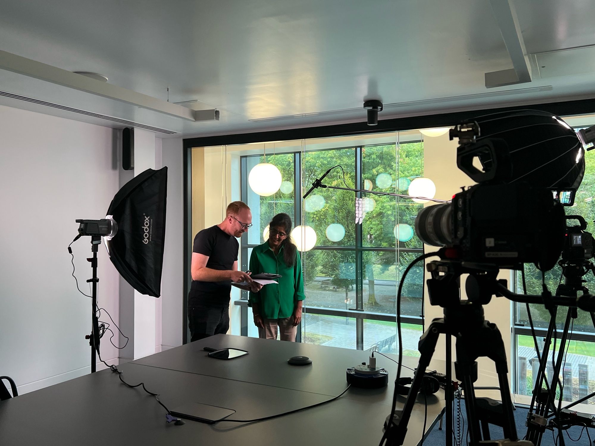 Fan from Adarak talks to Horizons Institute Business Support Officer Kuldip ahead of her interview slot. They are both stood in front of cameras and lights.