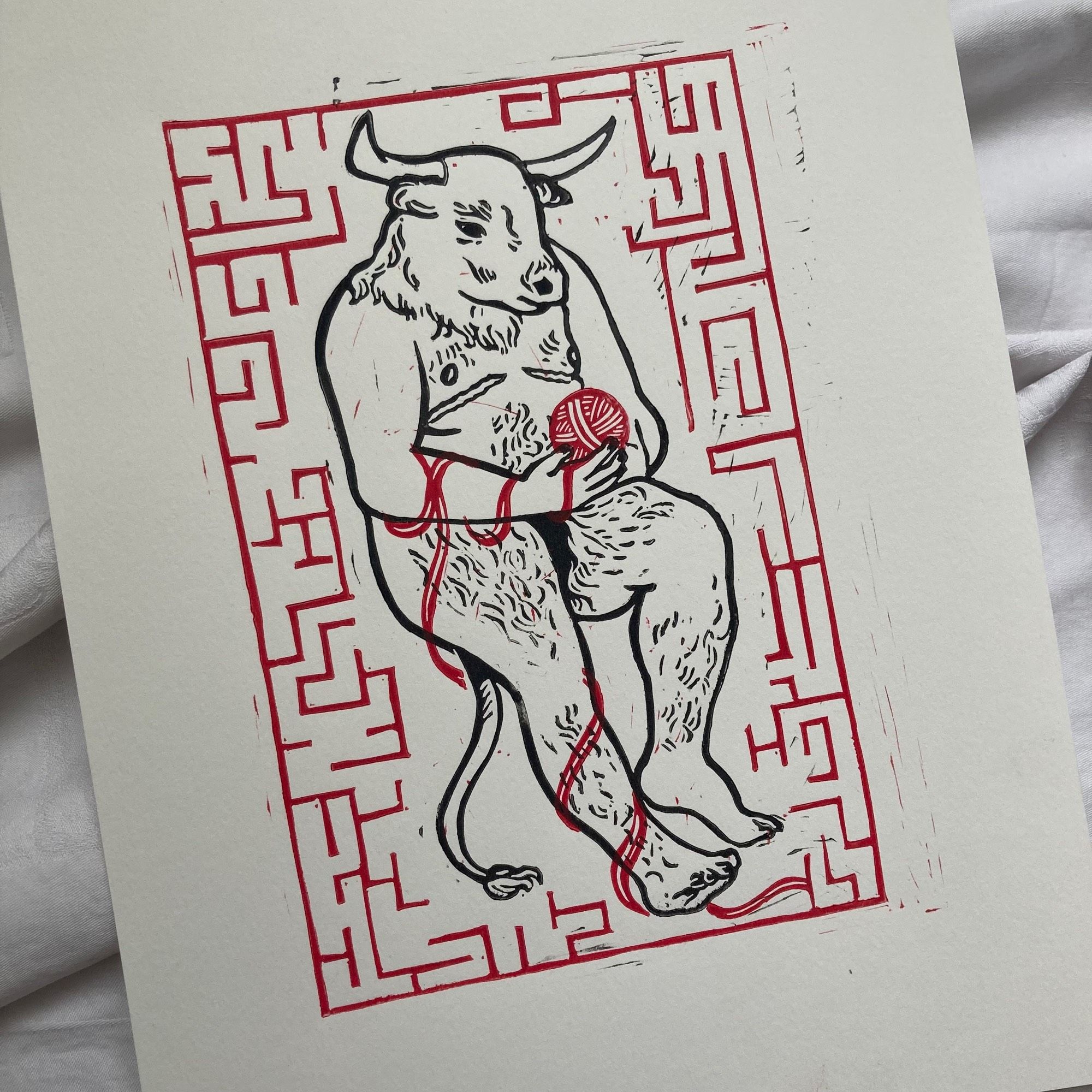 A two-layer red and black lino print of a minotaur. He has the body of a trans man with visible top surgery scars and the head of a cow. He is holding a ball of red yarn and is surrounded by a red maze.